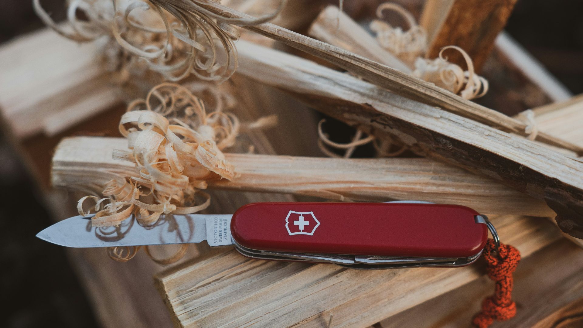 a red pocket knife sitting on top of a pile of wood
