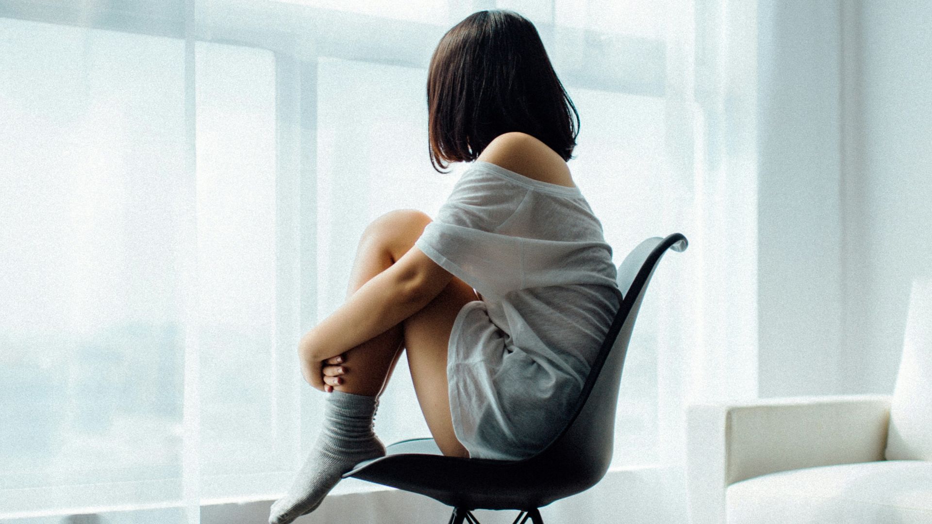 woman sitting on black chair in front of glass-panel window with white curtains