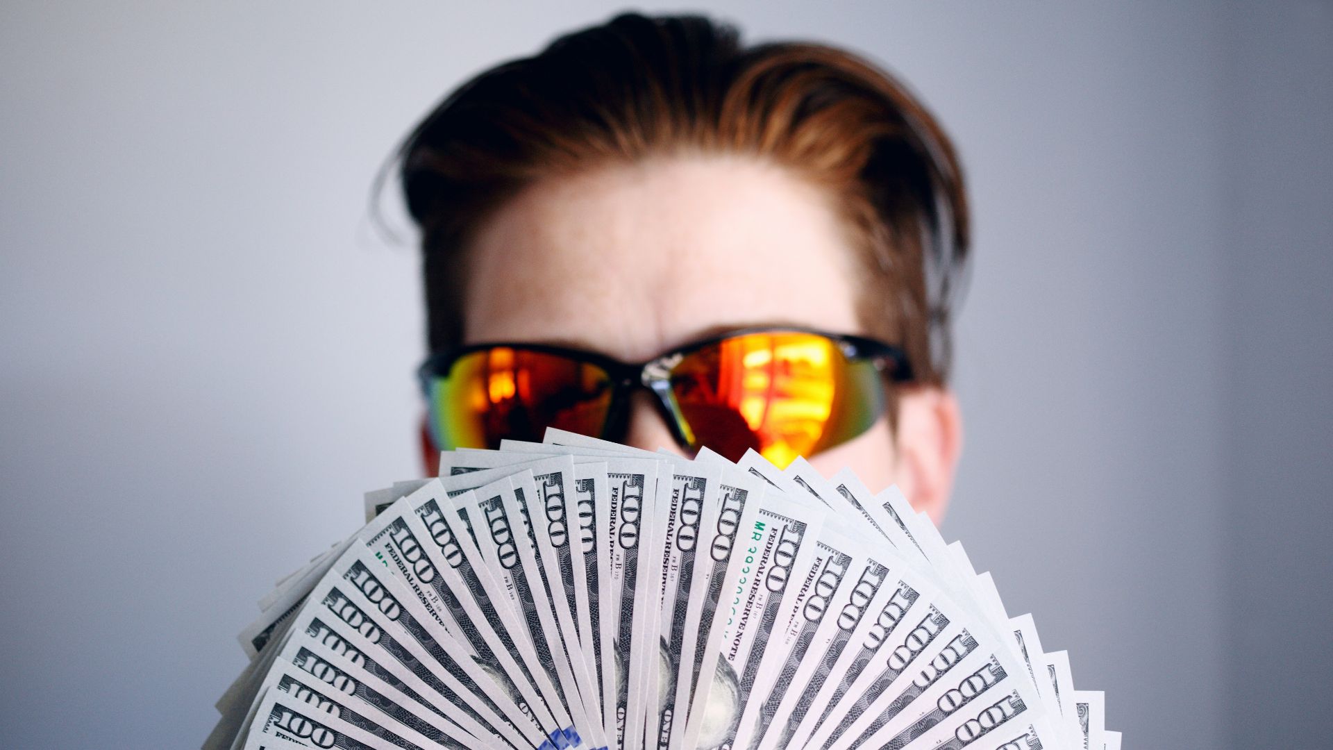 man in black framed sunglasses holding fan of white and gray striped cards
