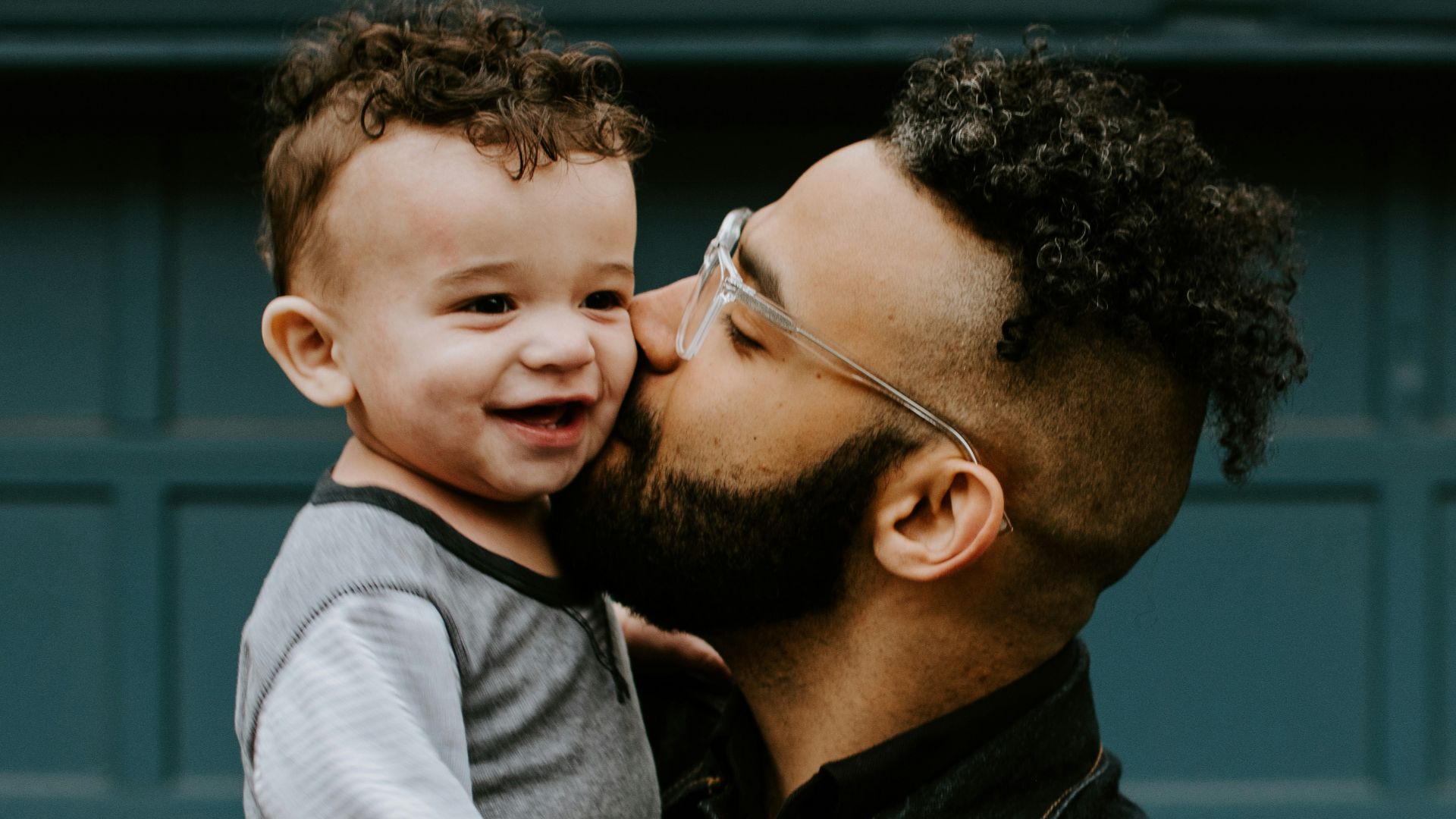 man carrying baby boy and kissing on cheek