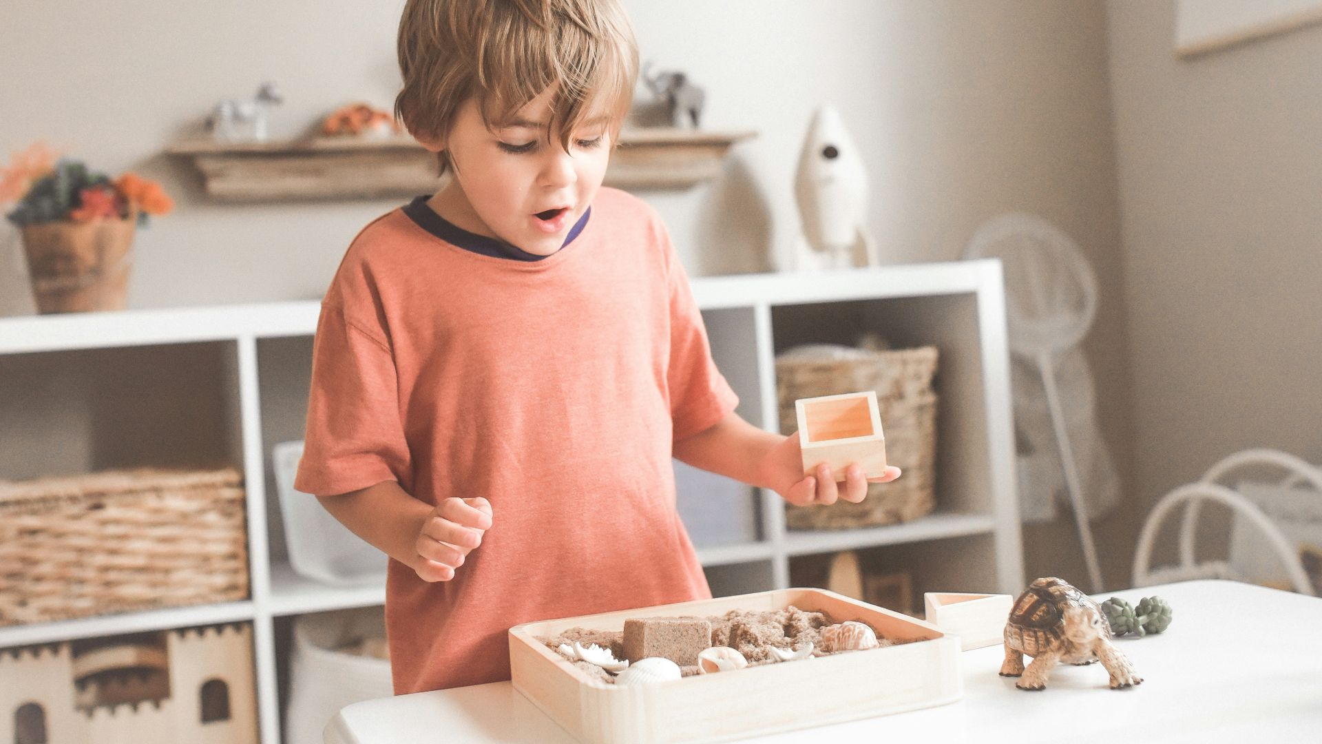 boy in orange crew neck t-shirt standing in front of white wooden table with cupcakes