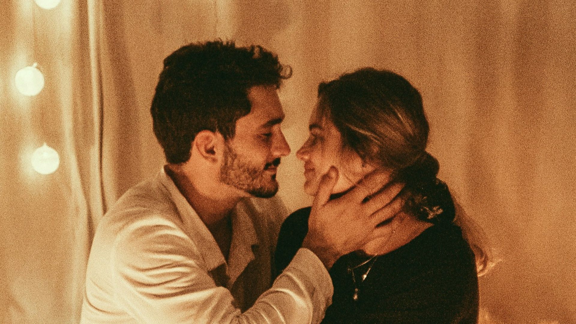 man and woman sitting on floor and about to kiss with lighted candles inside room