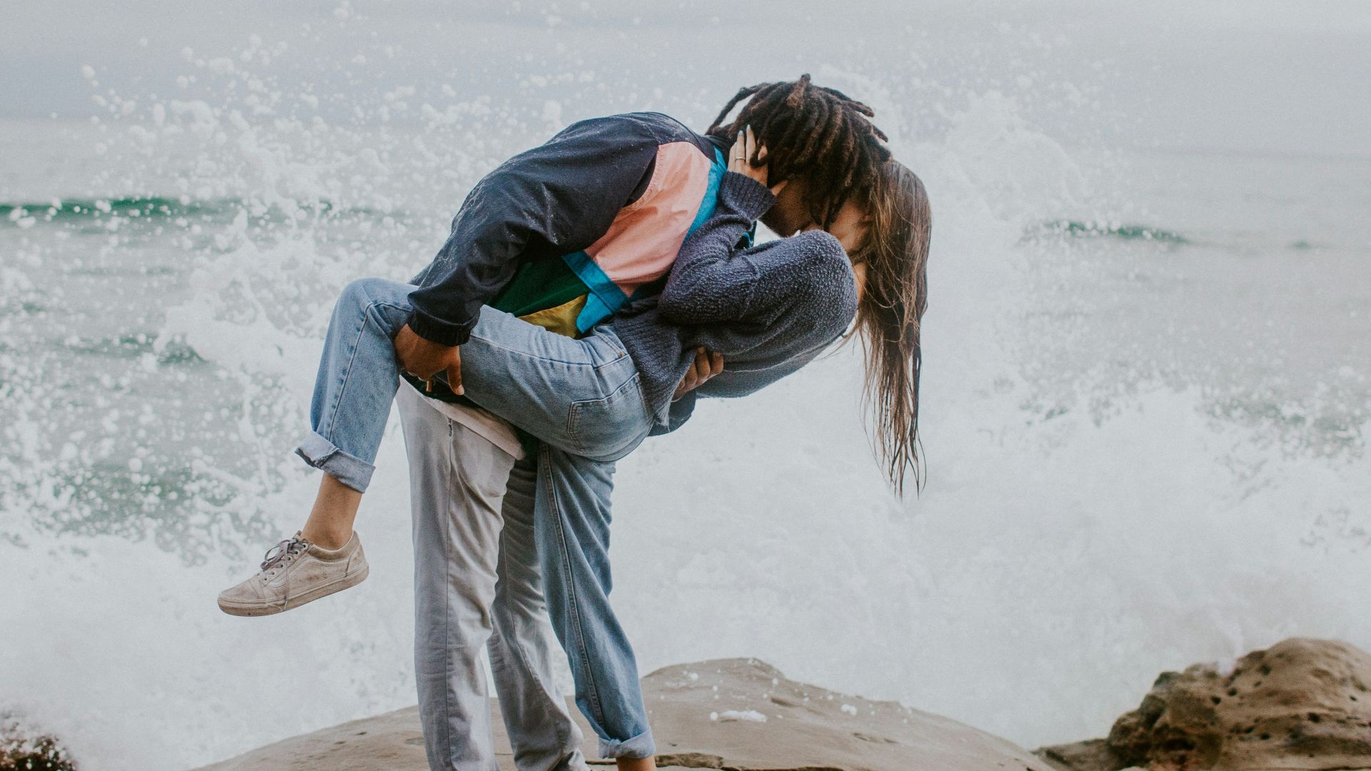 woman in blue jacket and gray pants carrying woman in blue jacket on beach during daytime