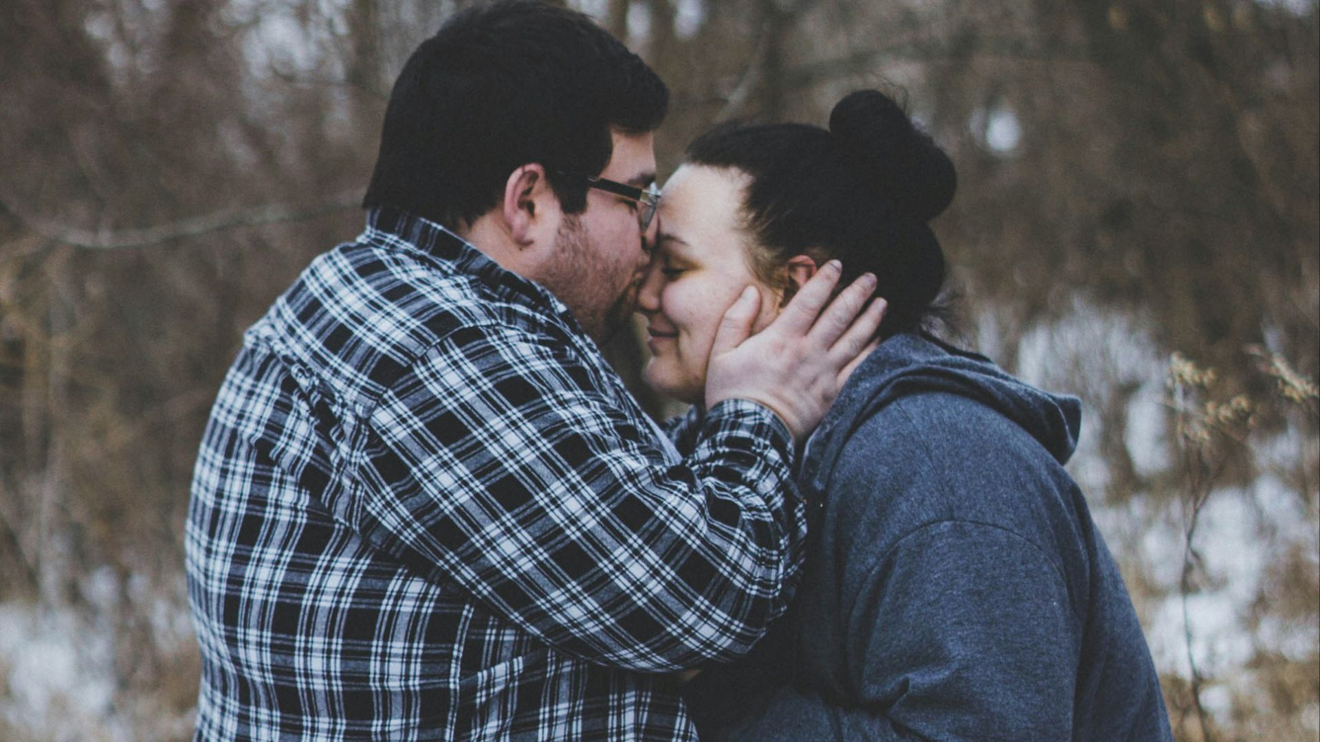 man kissing woman while standing near trees during daytime