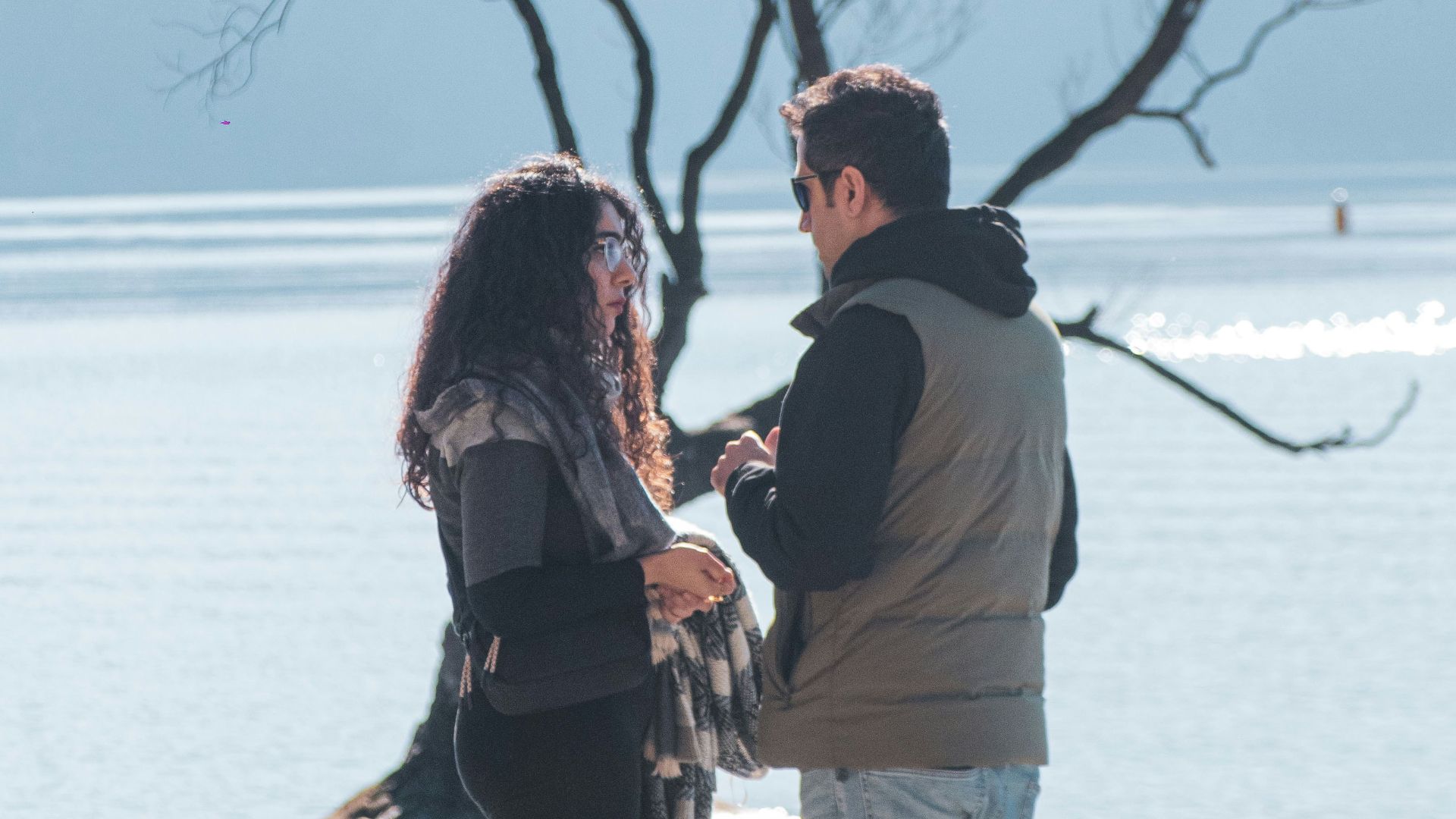 A man and woman standing on a beach next to a tree