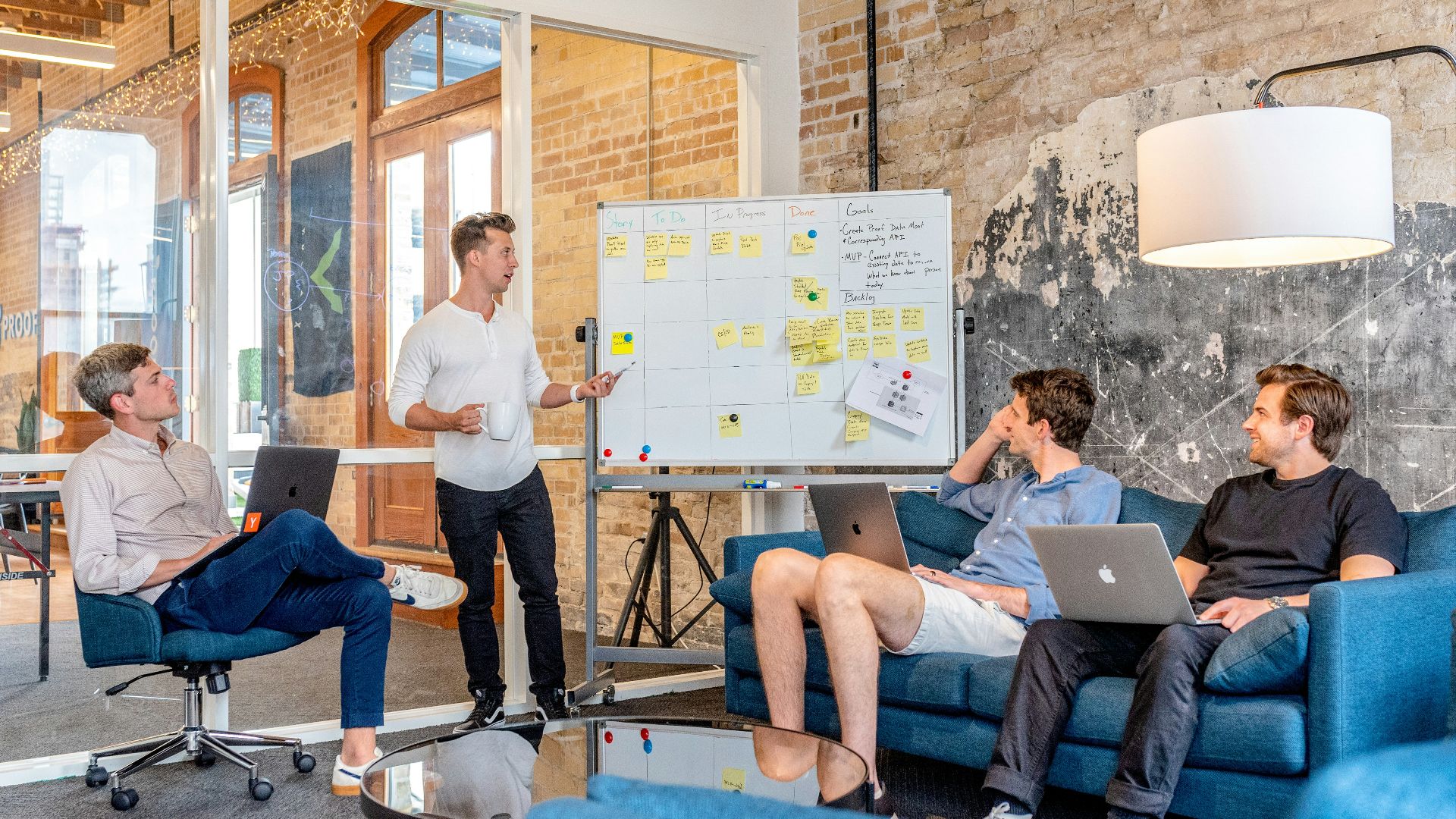 three men sitting while using laptops and watching man beside whiteboard