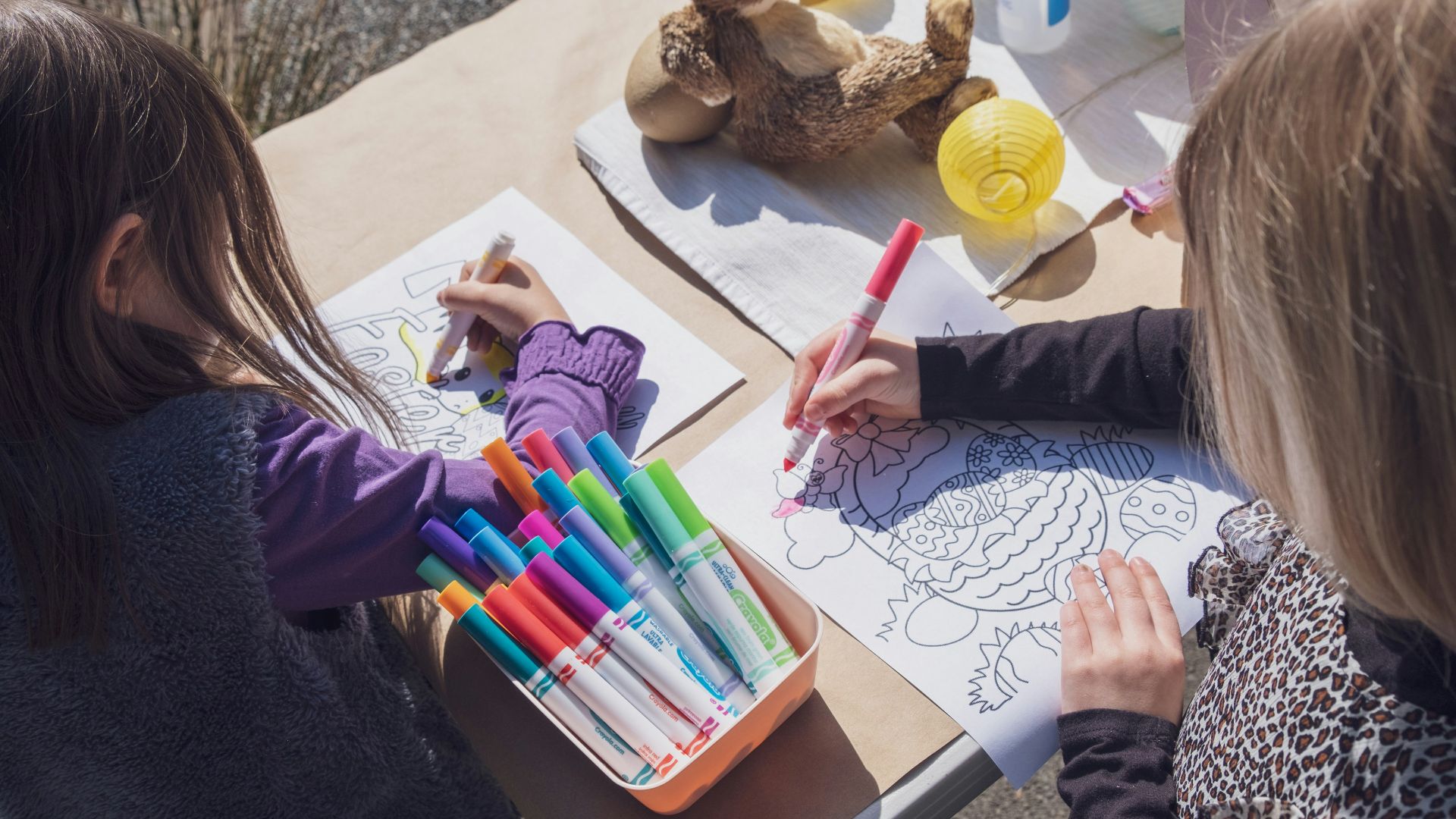 two young girls sitting at a table with markers and crayons