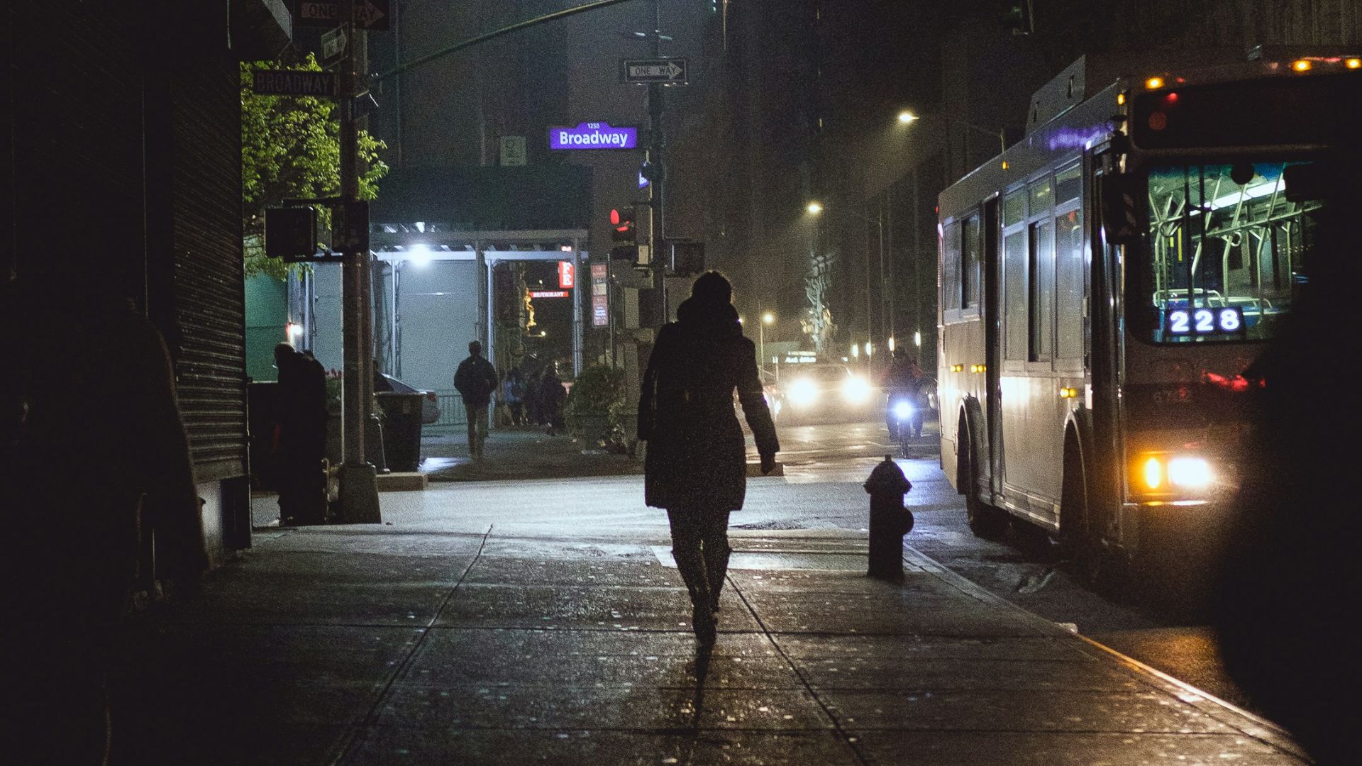 person walking on pathway near bus and vehicles during night time