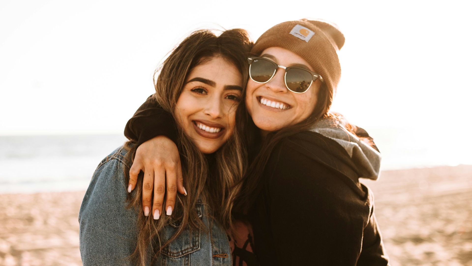 woman hugging other woman while smiling at beach