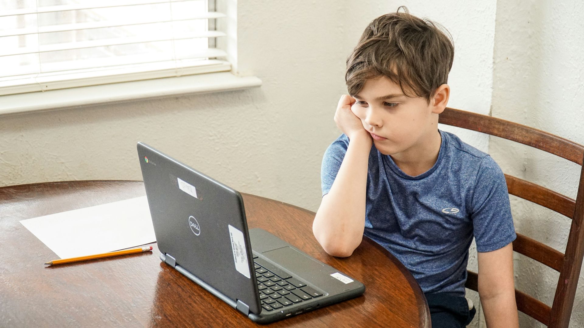 boy in blue crew neck t-shirt using macbook pro on brown wooden table