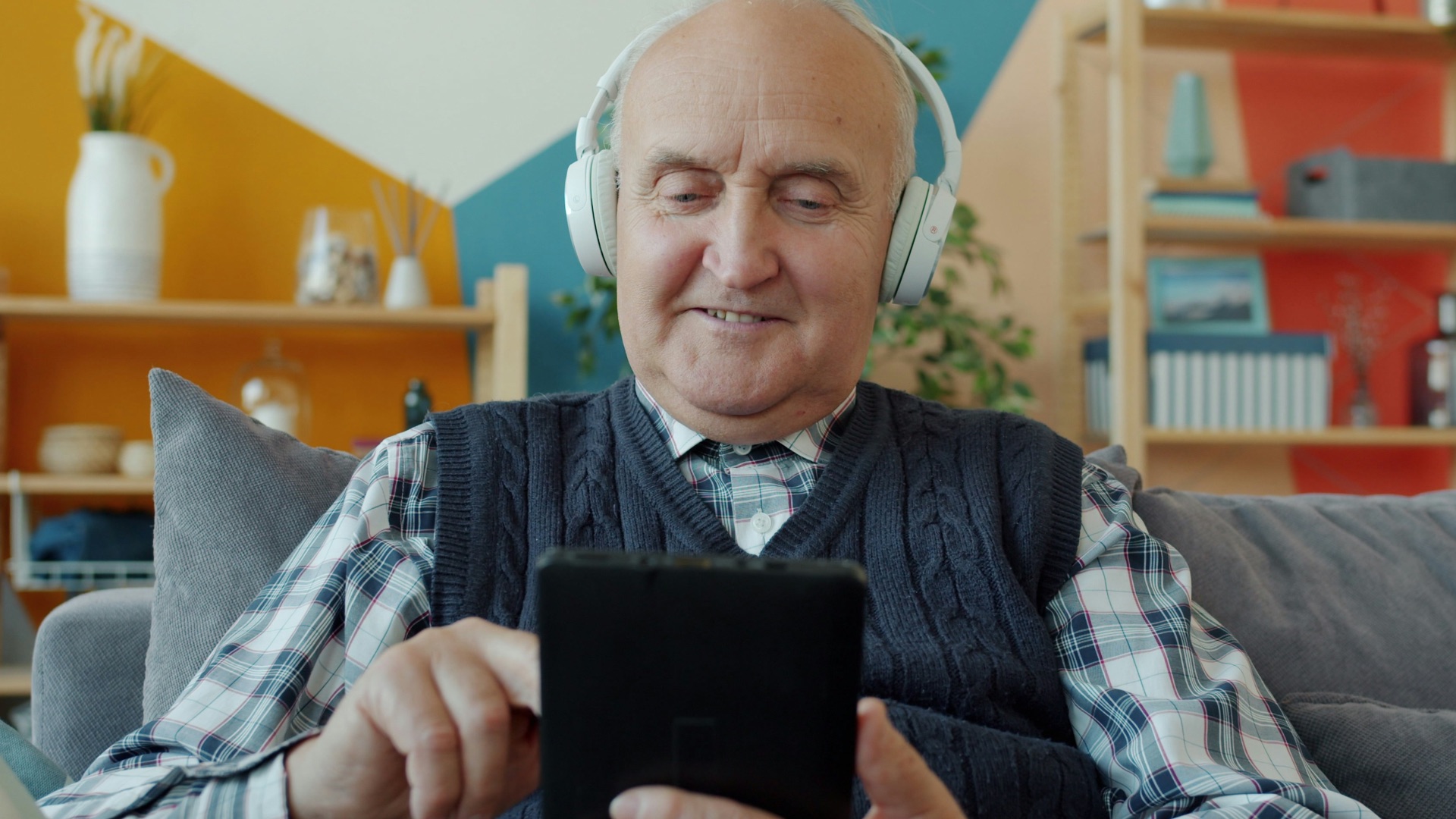 Elderly man with headphones uses a tablet.