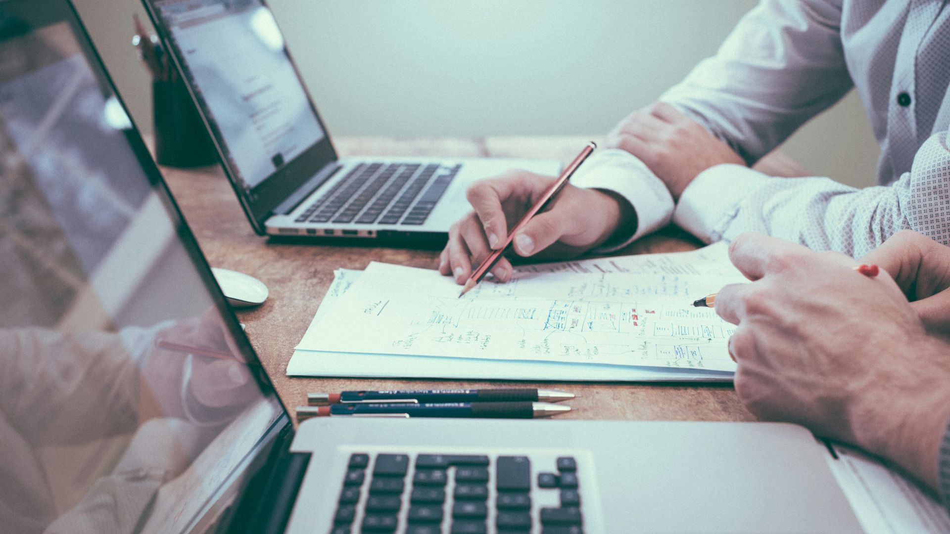 person holding pencil near laptop computer