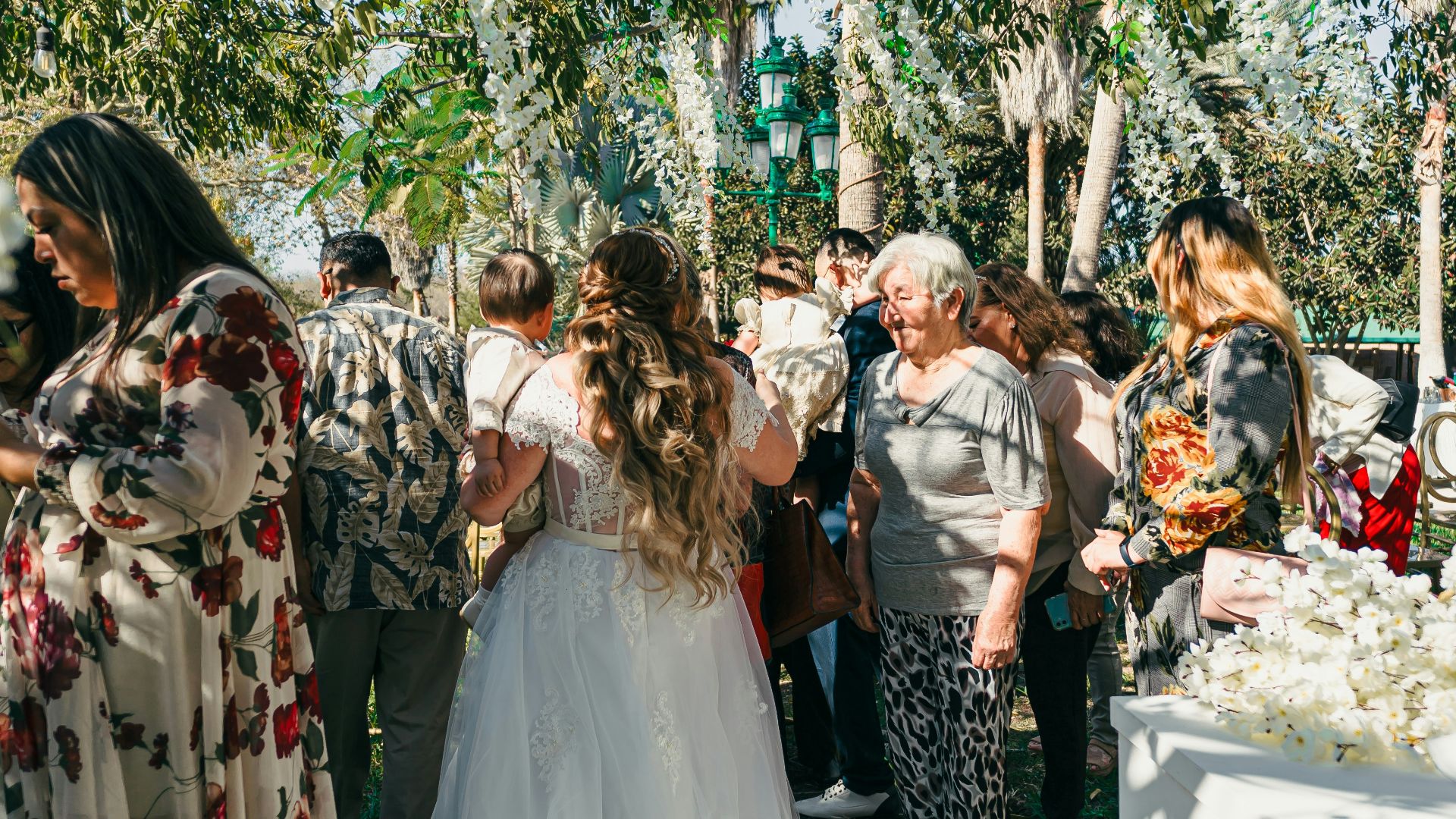 Bride in a white dress walking with guests outdoors.
