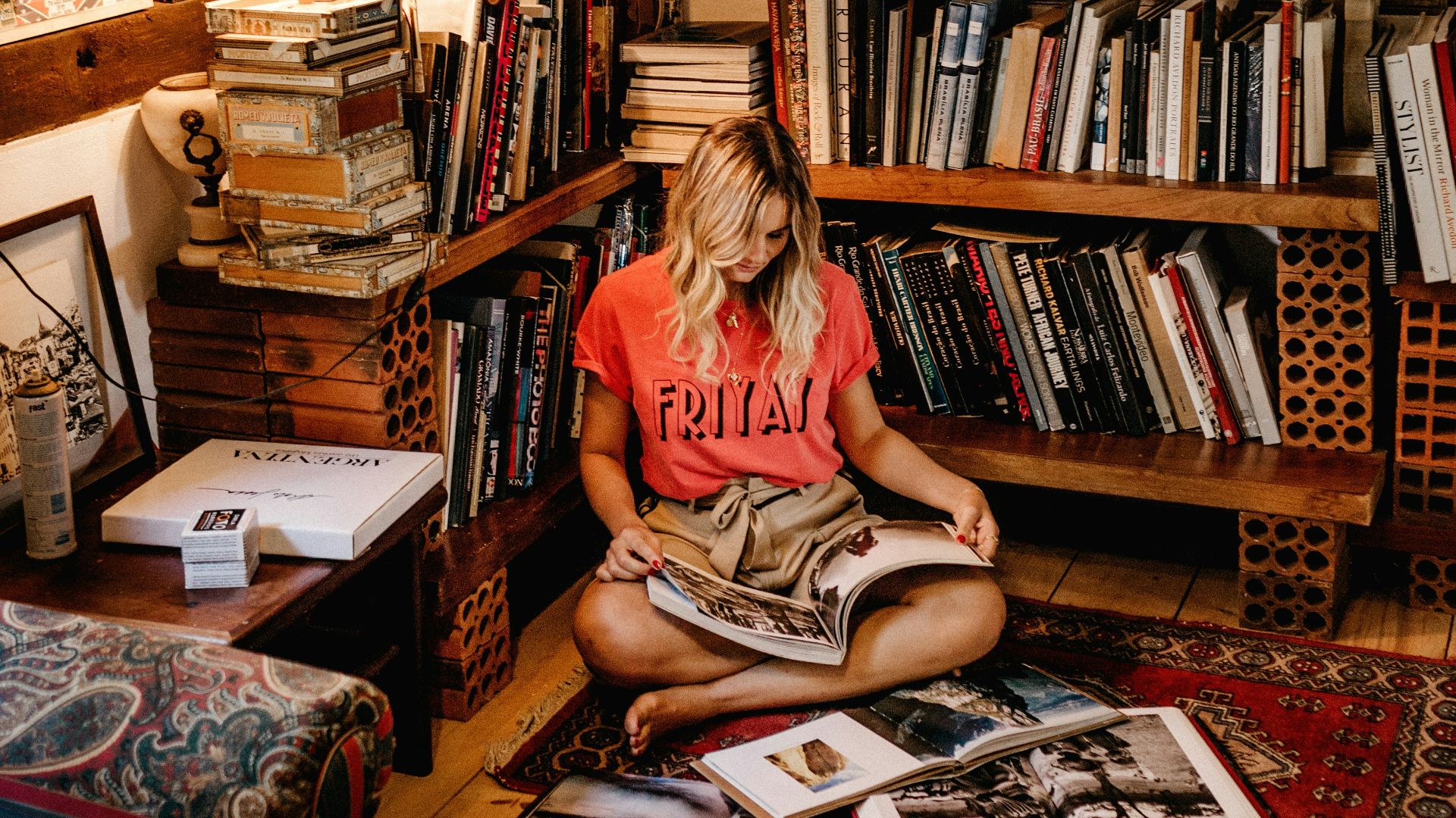 woman sitting on floor reading book in front of book case