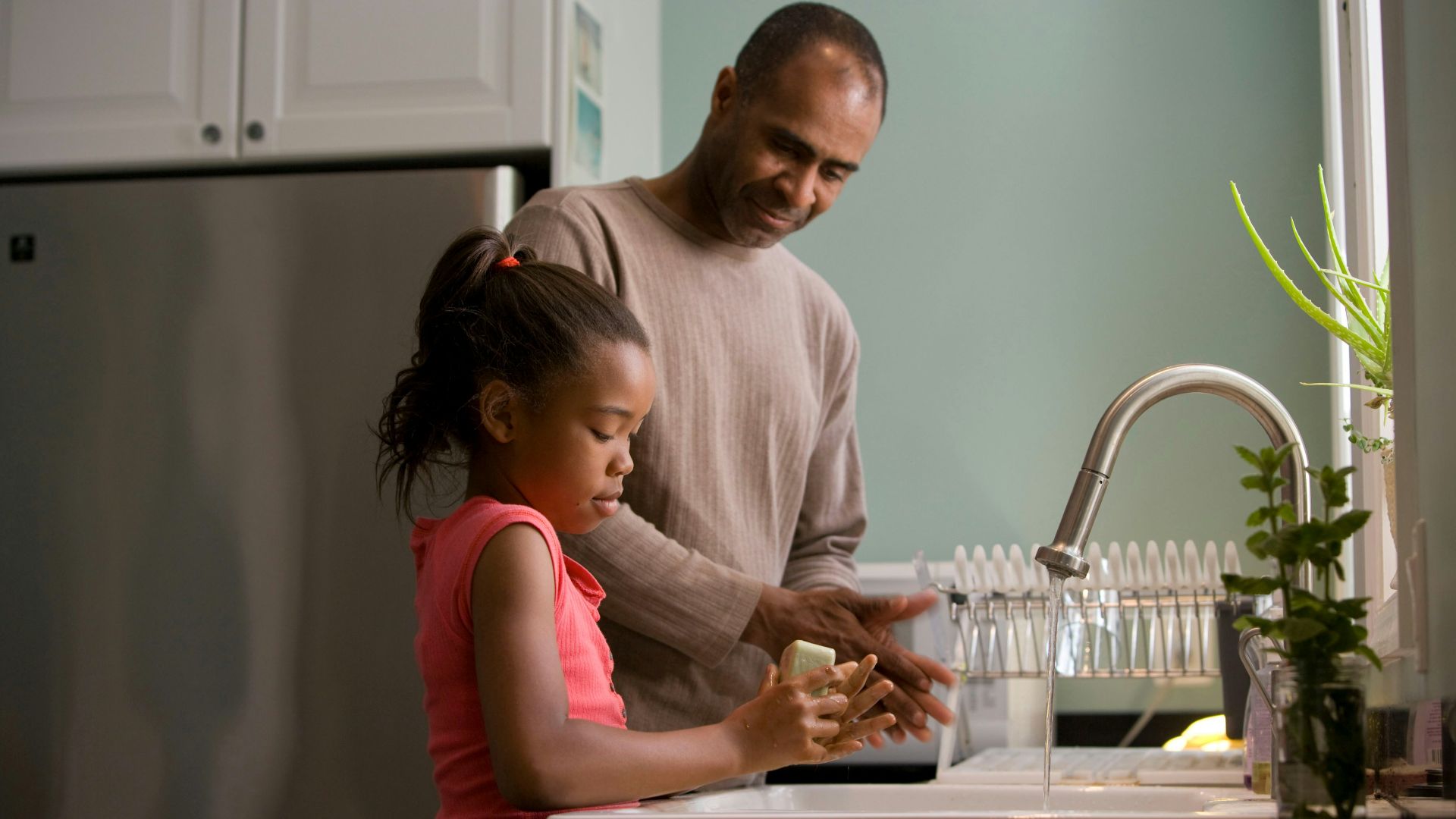 man in long sleeve shirt standing beside girl in pink tank top washing hands