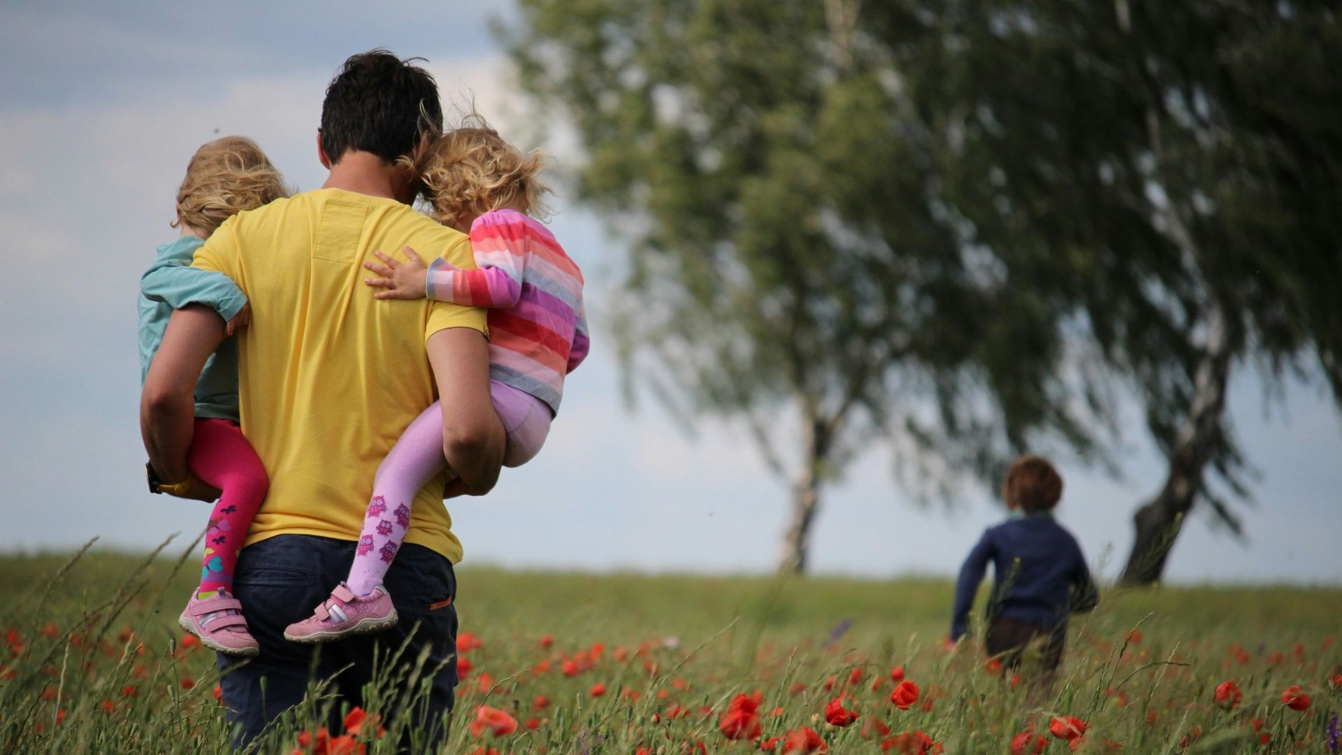 man carrying to girls on field of red petaled flower