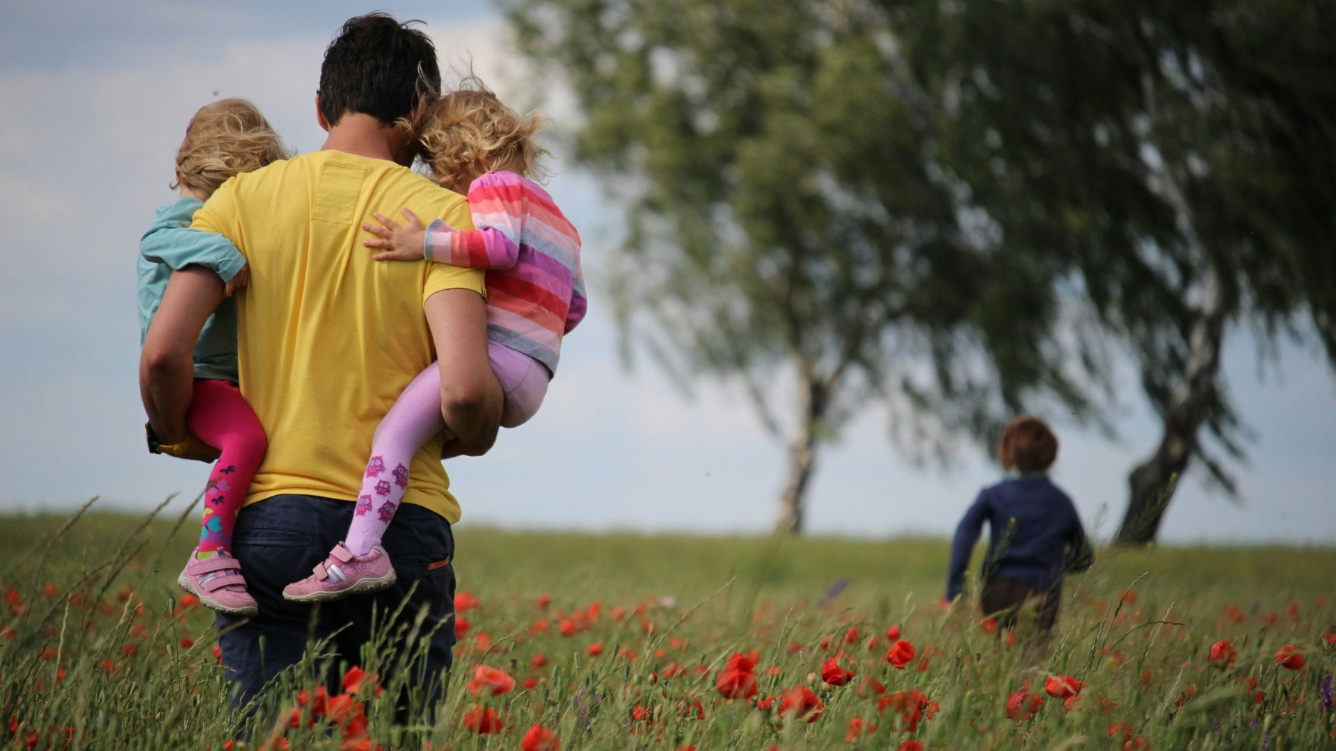 man carrying to girls on field of red petaled flower