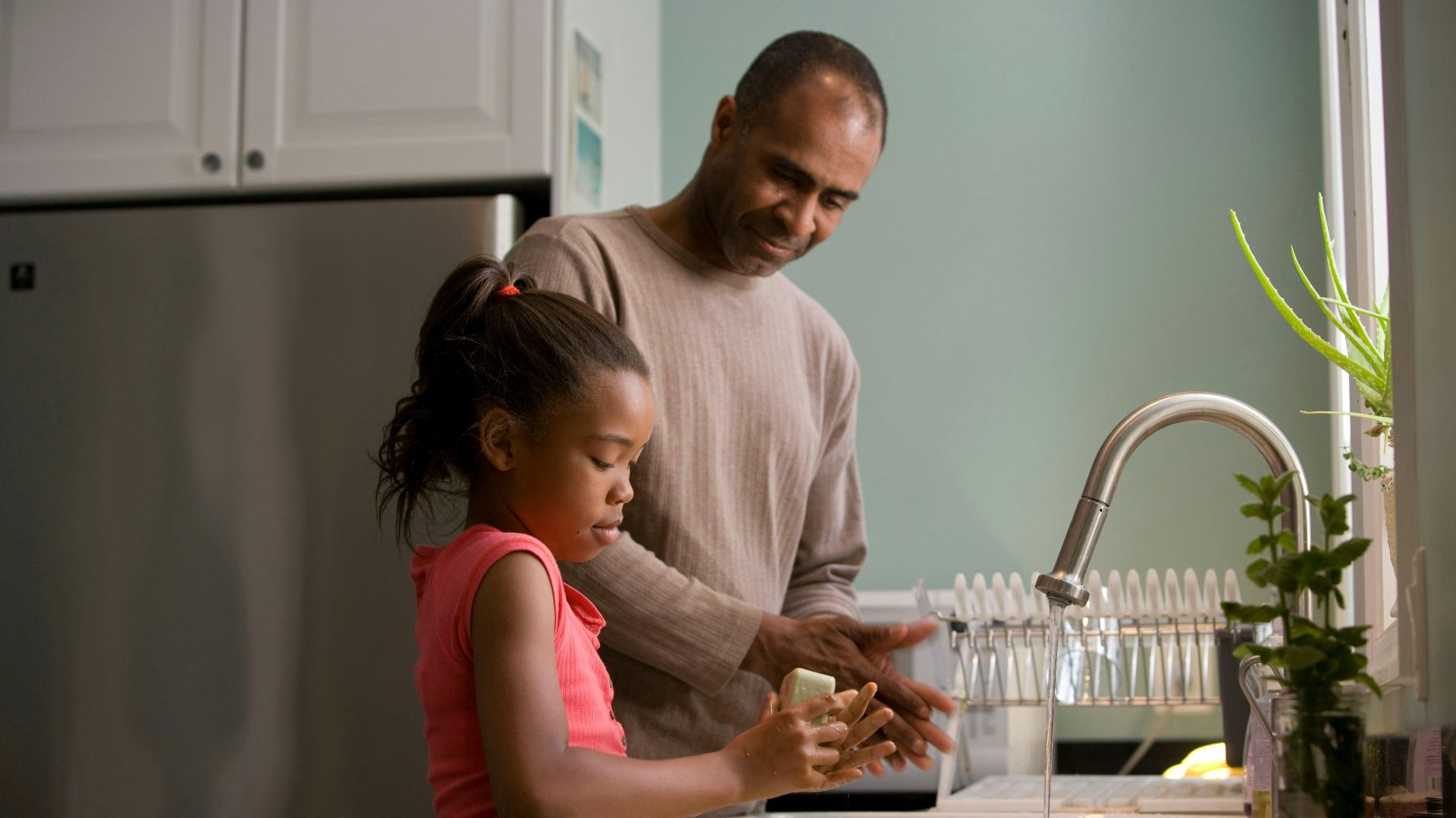 man in long sleeve shirt standing beside girl in pink tank top washing hands