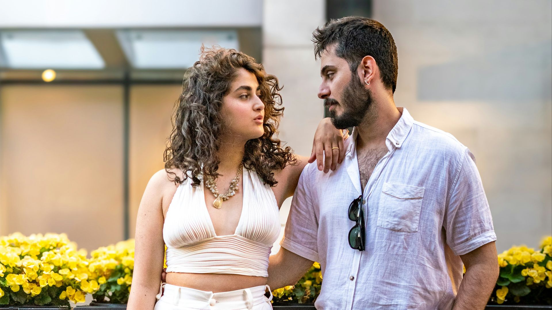A couple poses together outdoors, looking at each other.