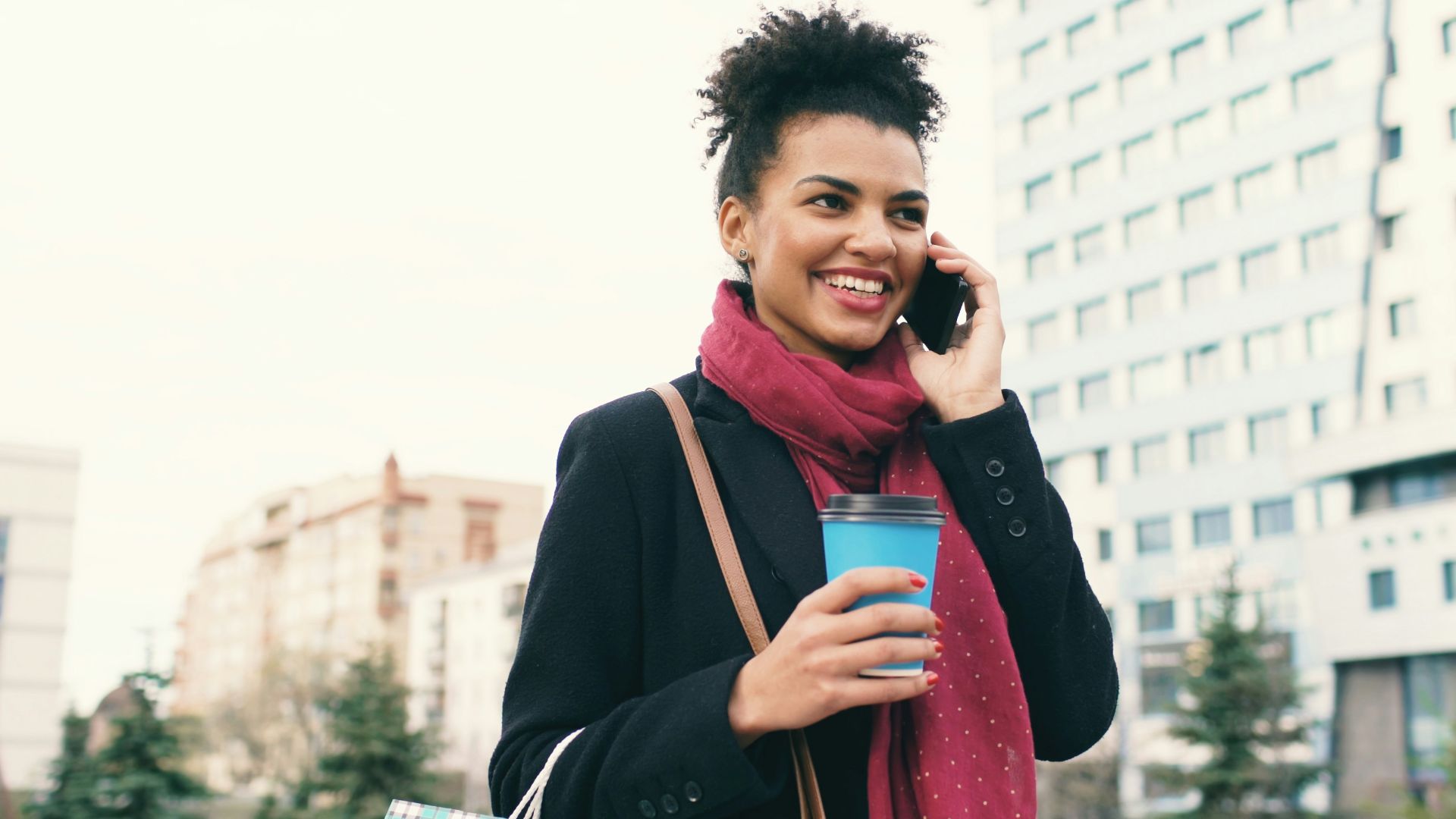 Woman talking on phone holding coffee and shopping bags