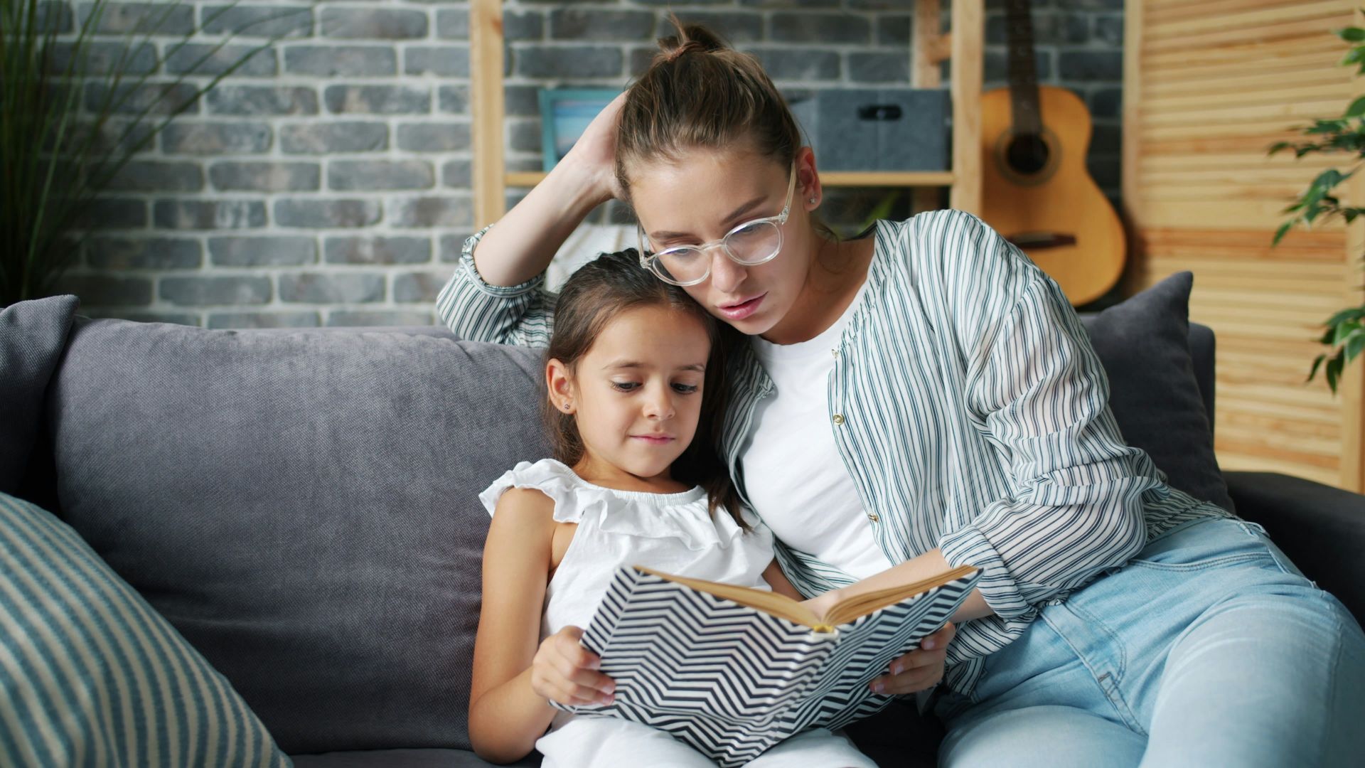 Mother and daughter reading a book together on couch
