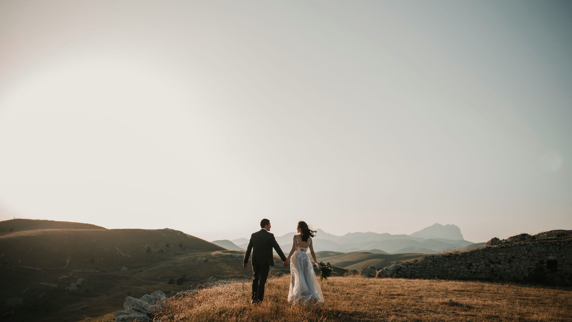 a bride and groom walking on a hill