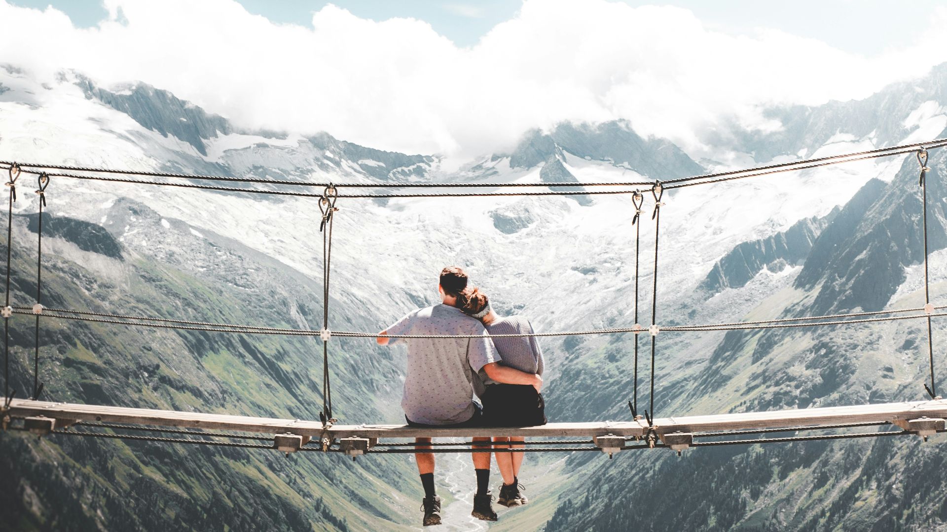 man and woman sitting on hanging bridge at daytime