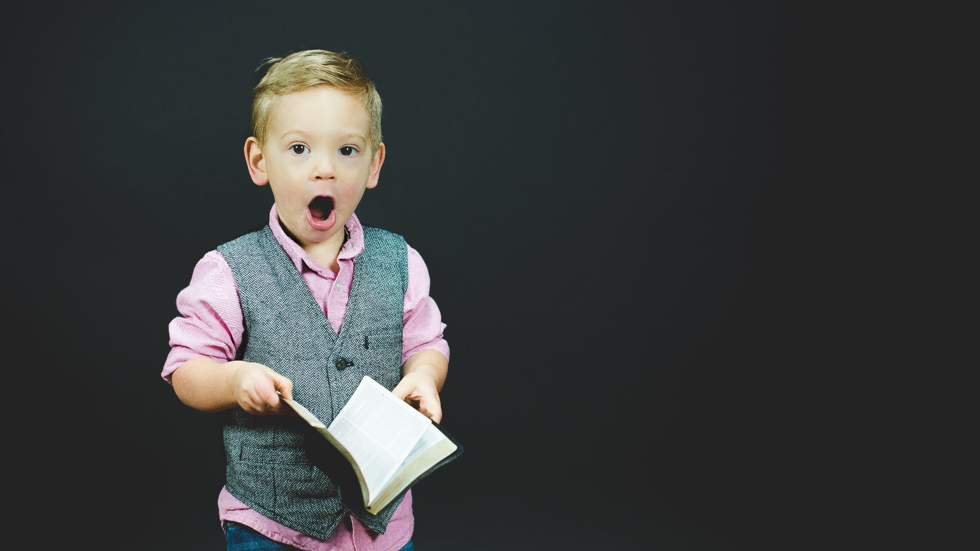 boy wearing gray vest and pink dress shirt holding book