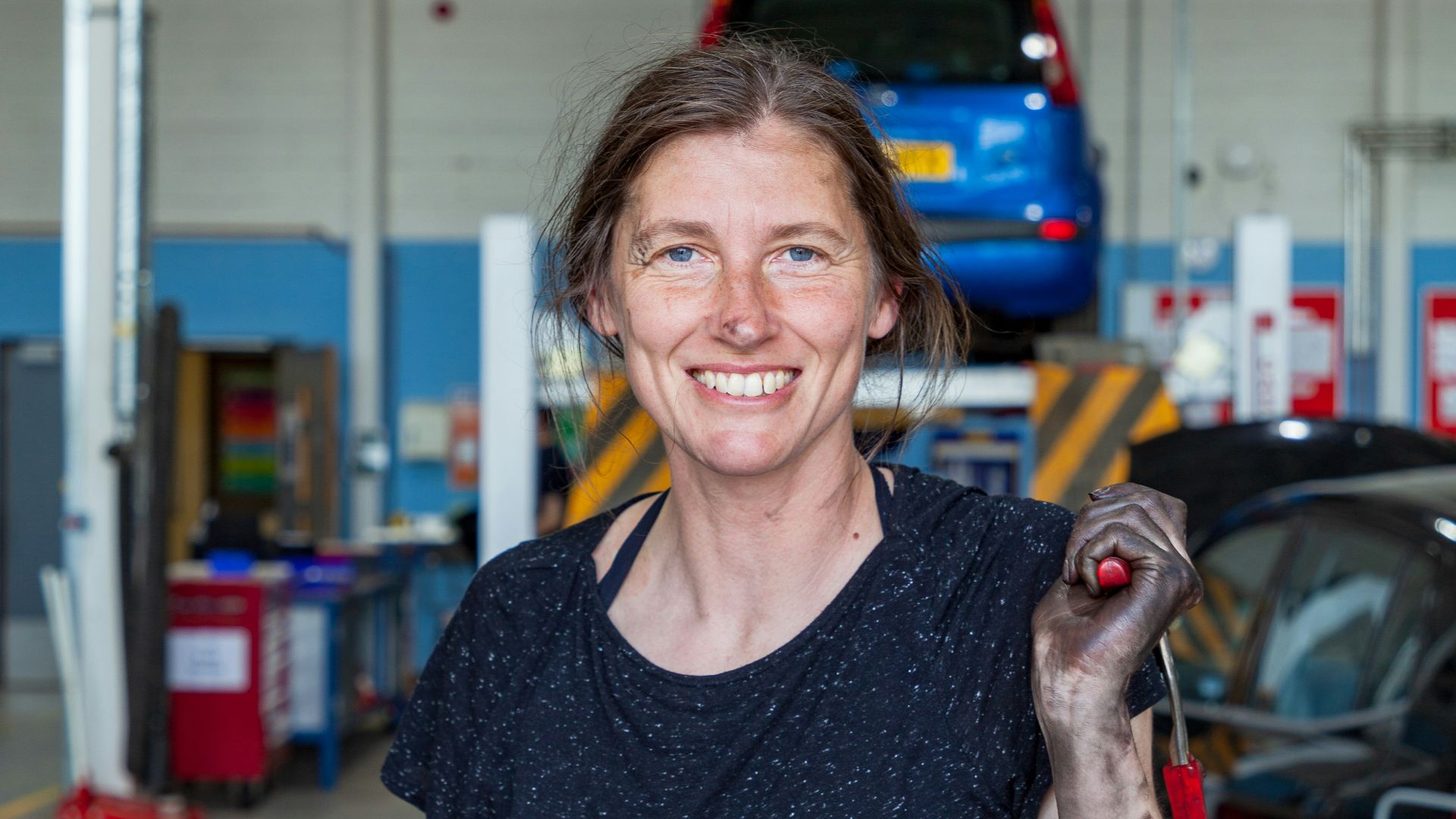 a woman holding a wrench in a garage