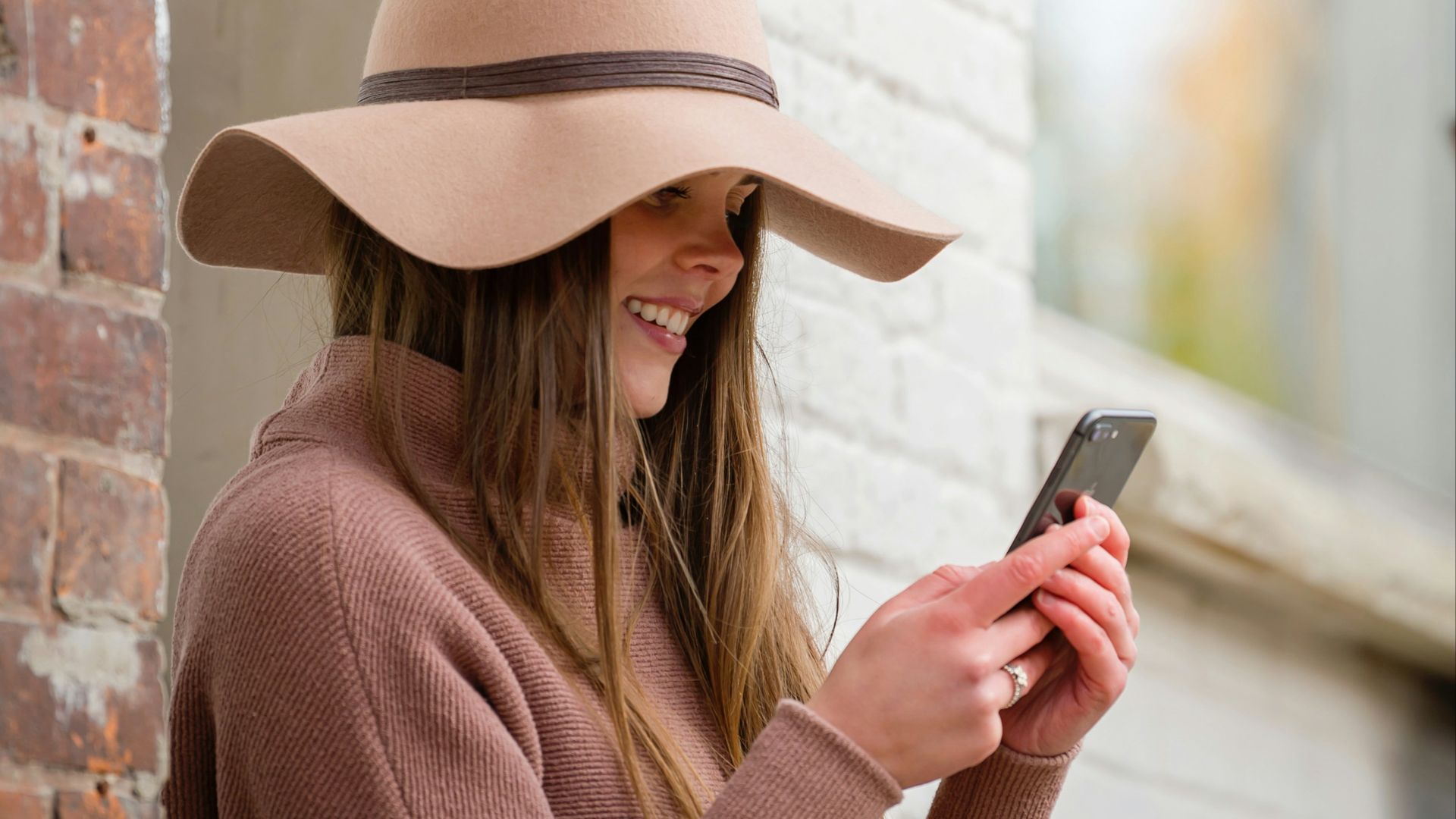 woman in brown hat and brown sweater holding smartphone