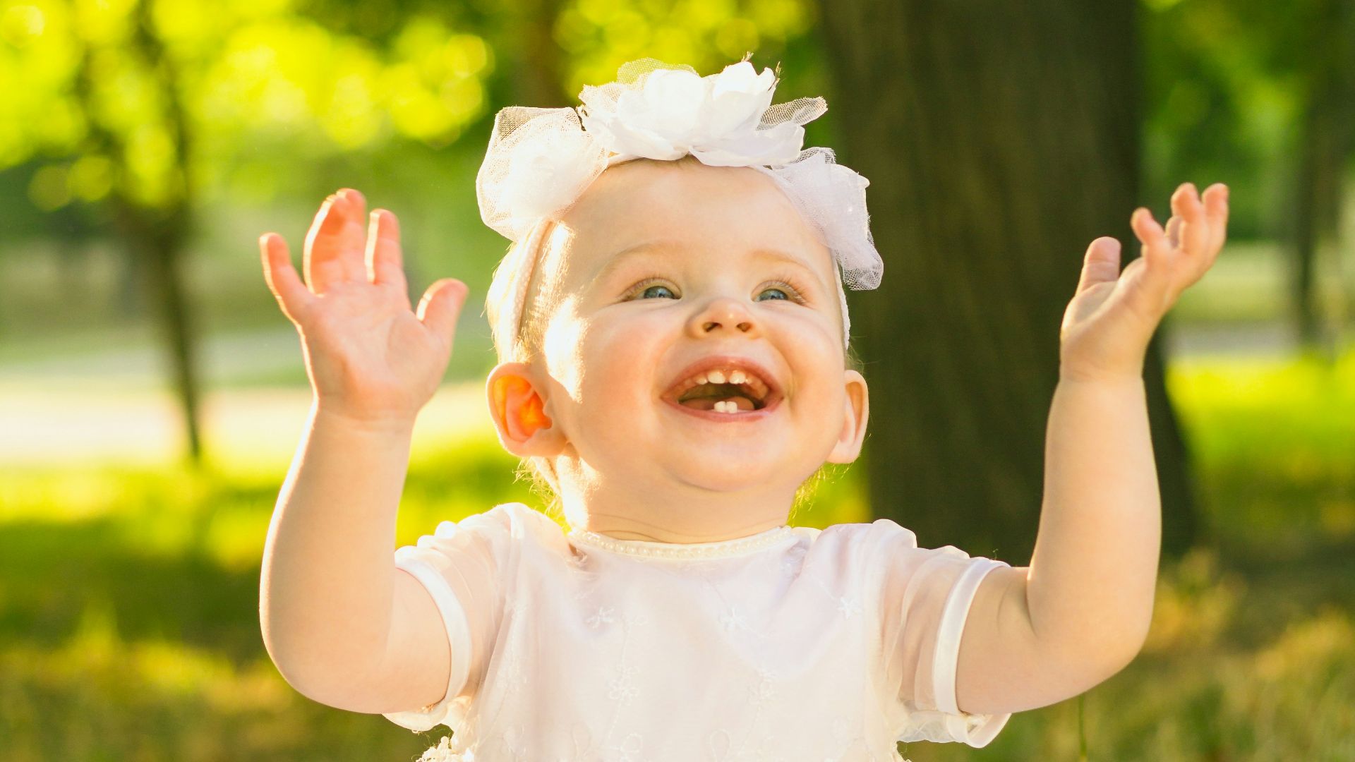 a baby girl in a white dress sitting in the grass