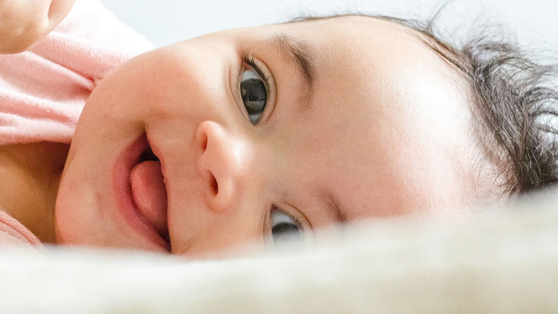 baby in pink shirt lying on white textile