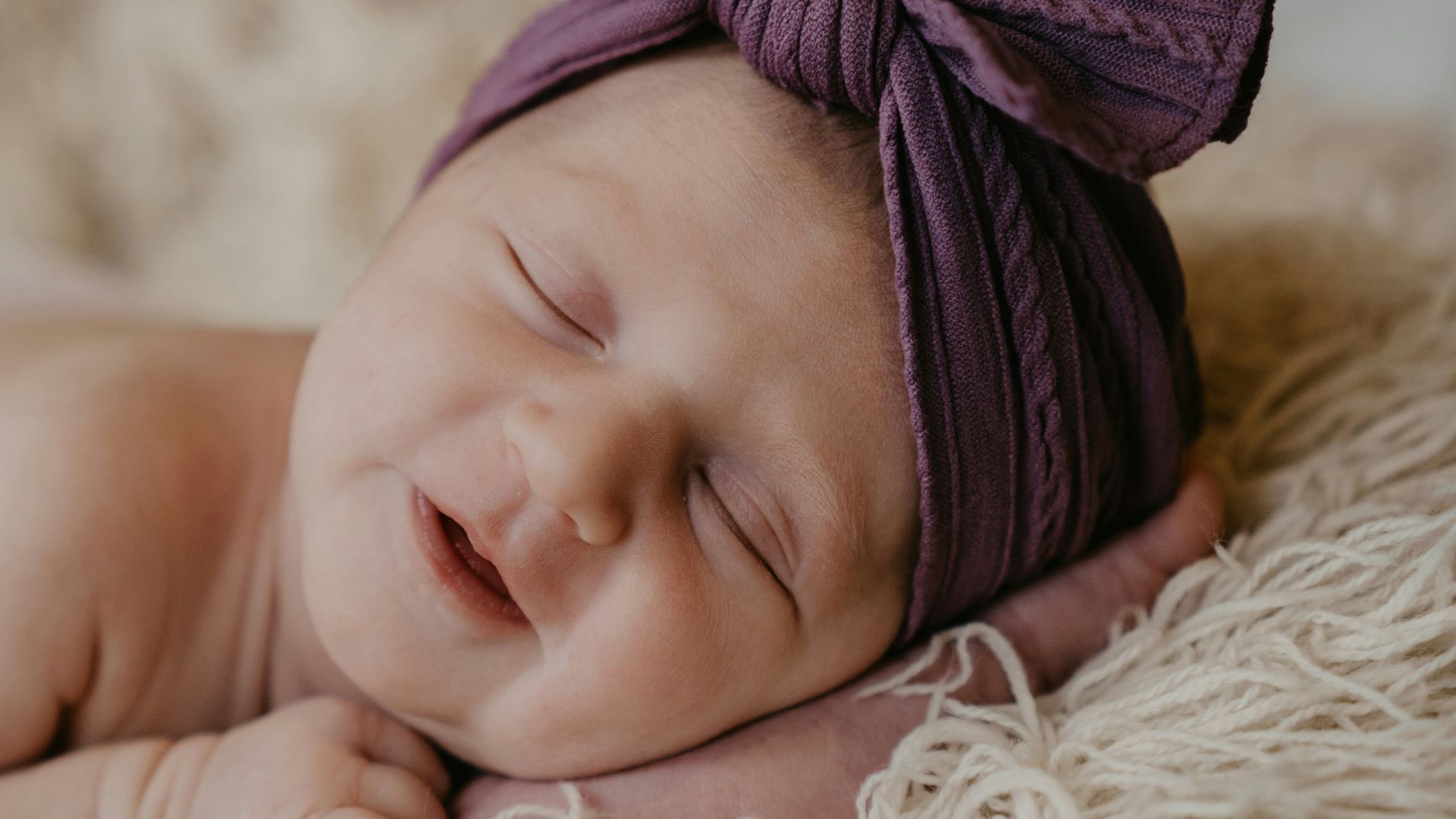 baby in purple knit cap lying on white fur textile