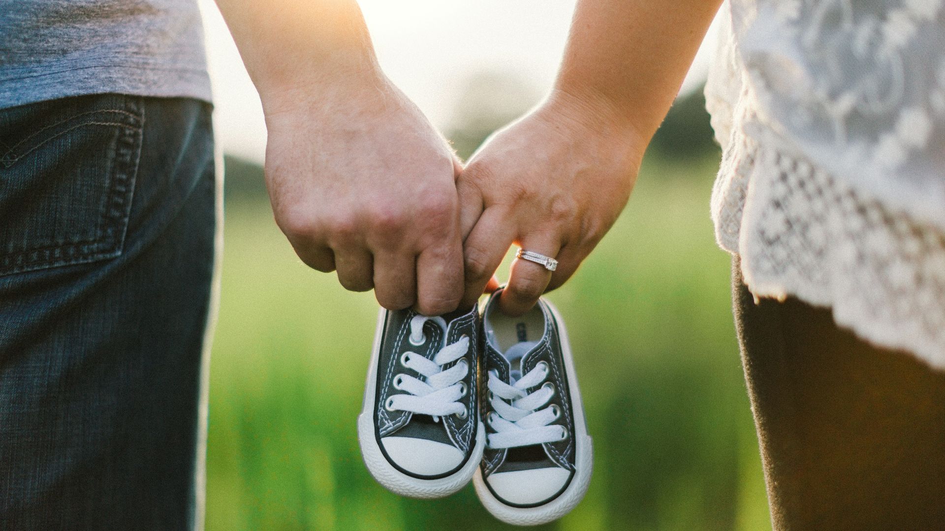 woman and man holding black crib shoes standing near green grass during daytime
