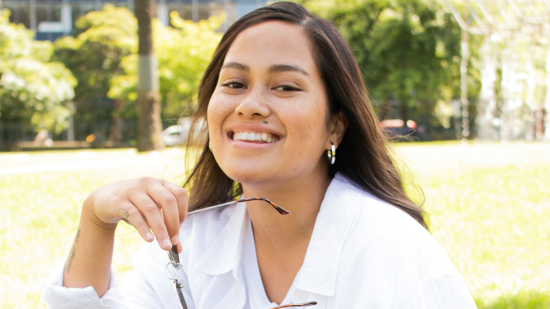 woman in white dress shirt and blue denim jeans sitting on green grass field during daytime