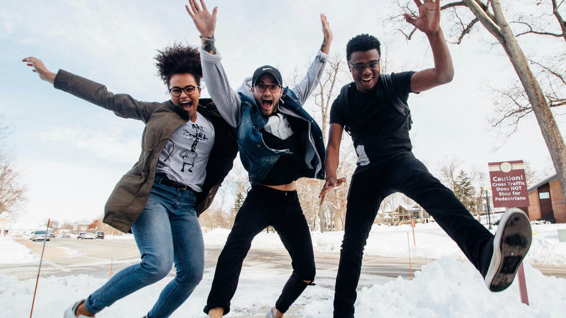 photo of three men jumping on ground near bare trees during daytime