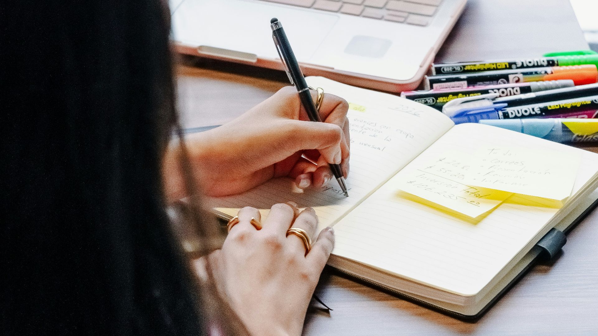 Person working on laptop and notebook at desk.