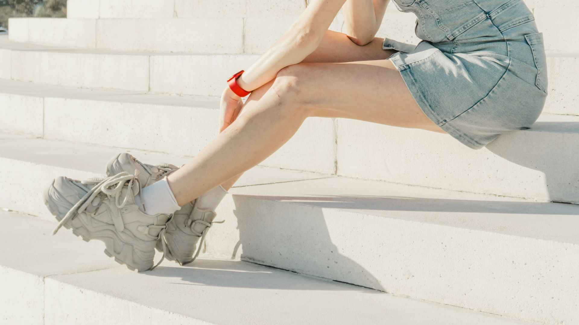 Young woman in denim dress sitting on white steps