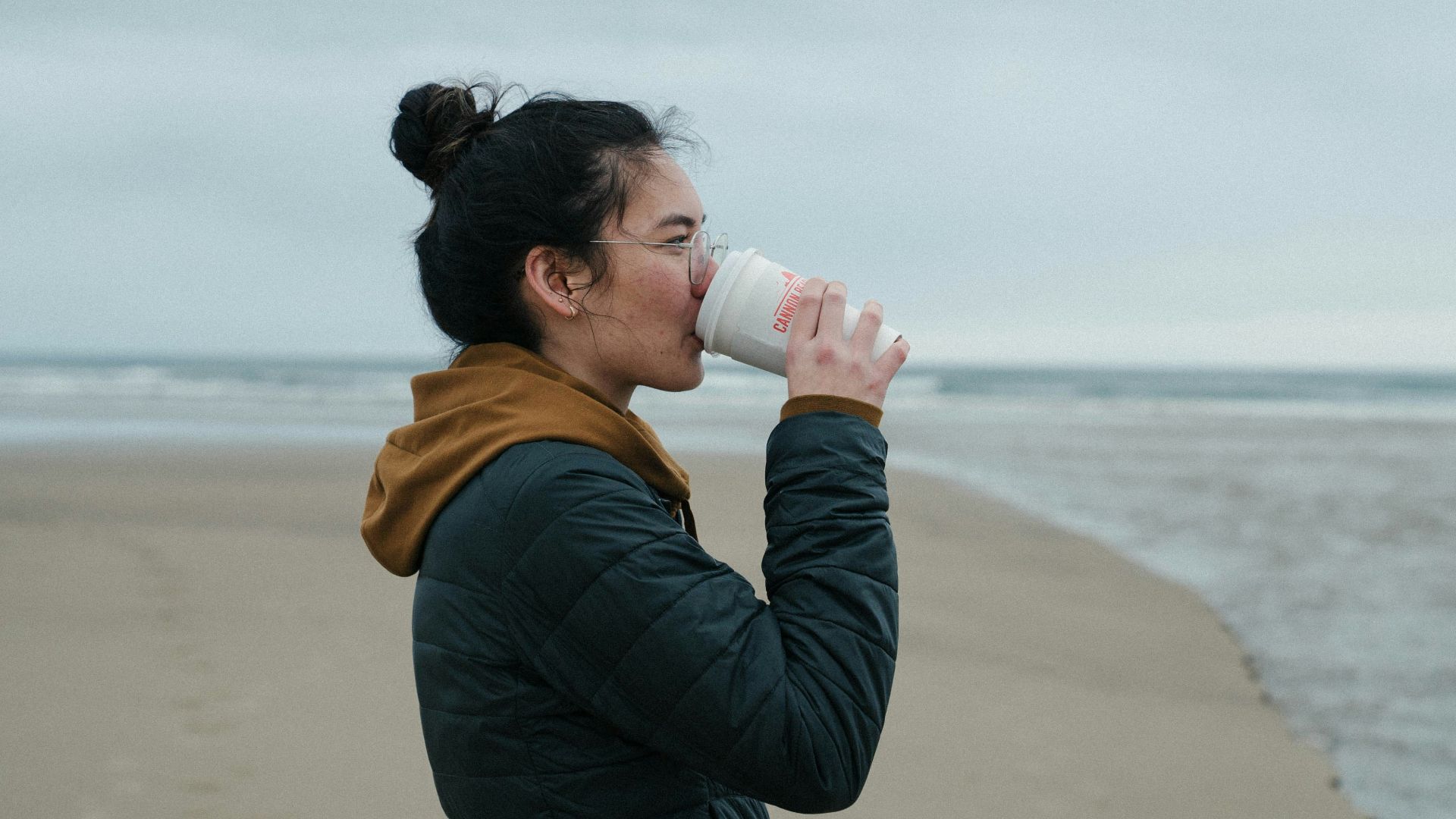 a woman drinking from a cup on the beach