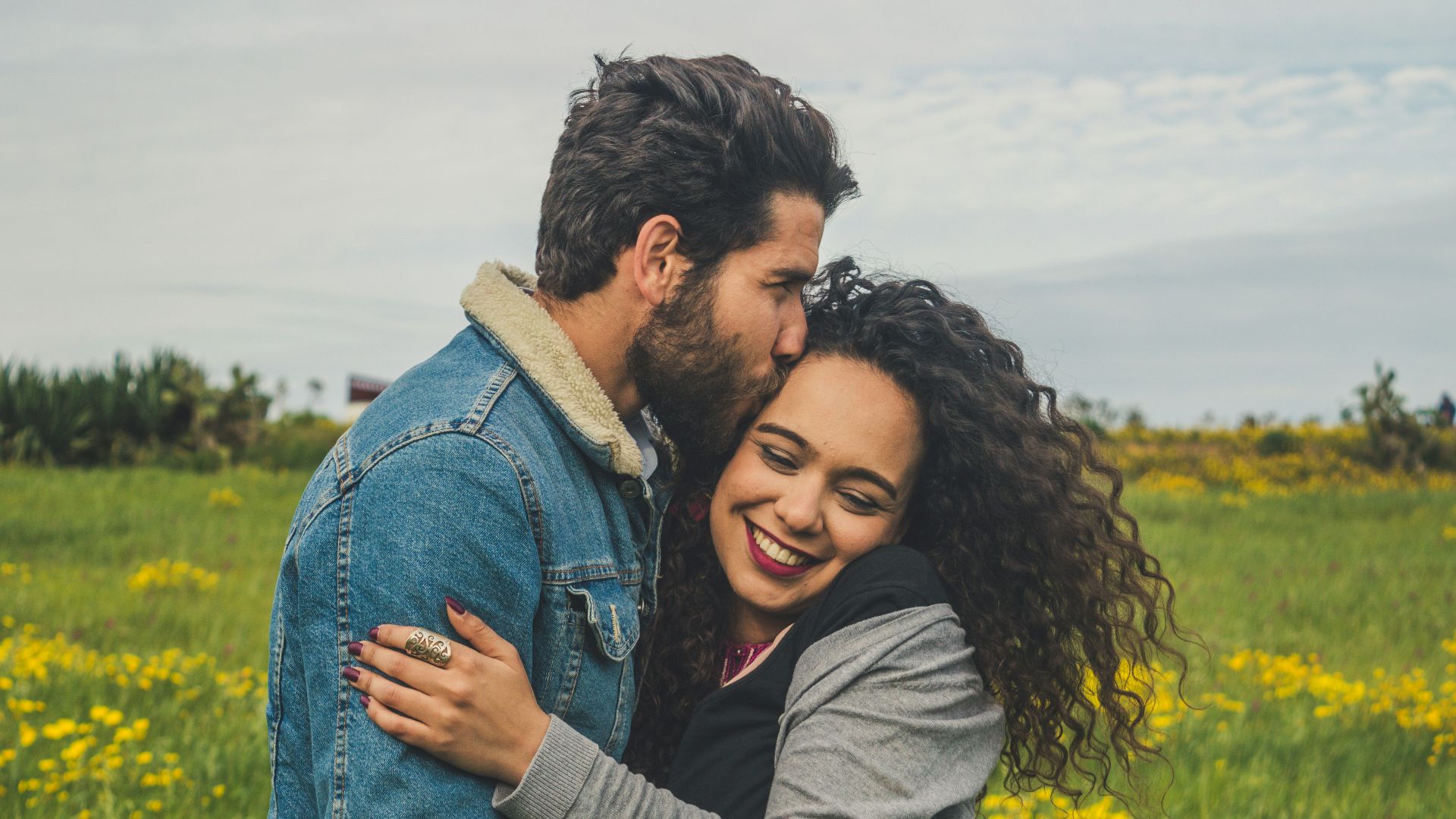 man kissing on woman's head on the green grassy field