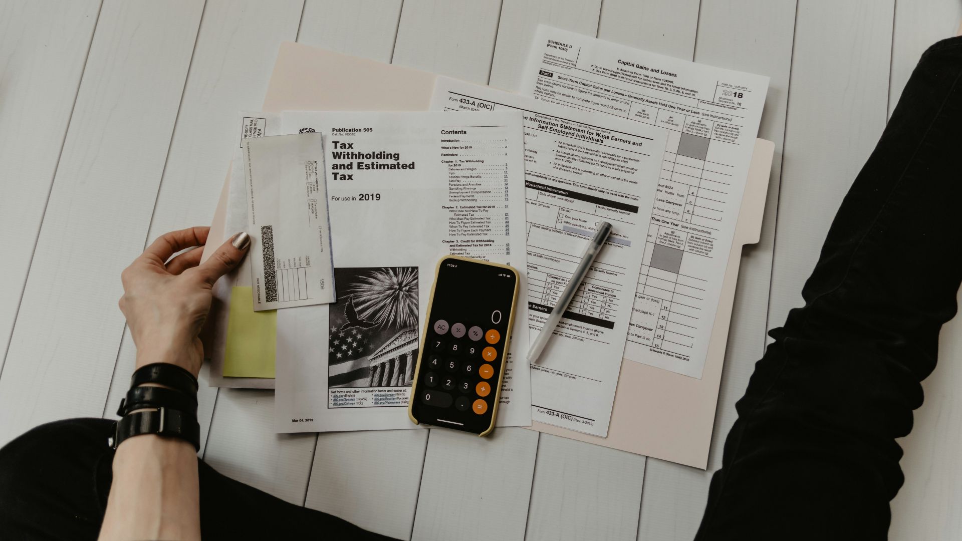 person holding paper near pen and calculator