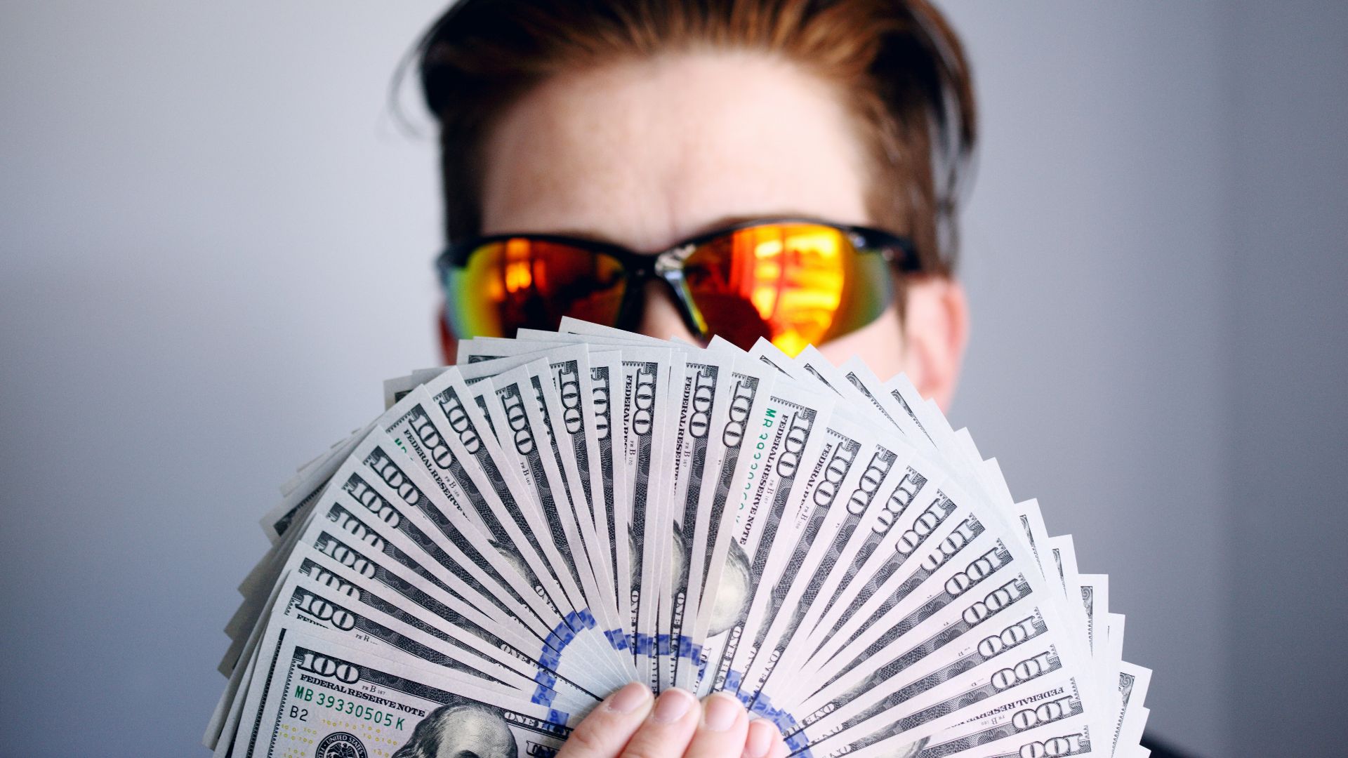 man in black framed sunglasses holding fan of white and gray striped cards