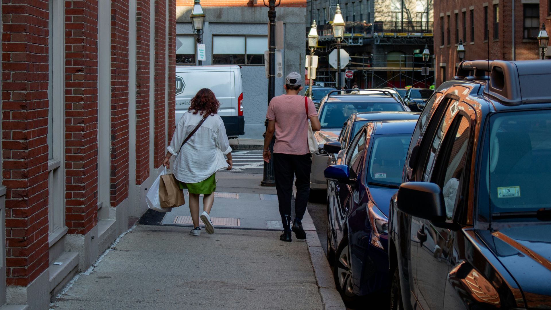 a couple of people walking down a sidewalk next to parked cars