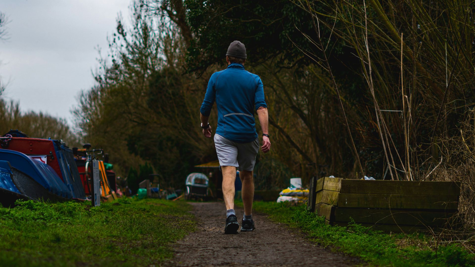 man in blue t-shirt and blue denim shorts standing on brown wooden bench during daytime
