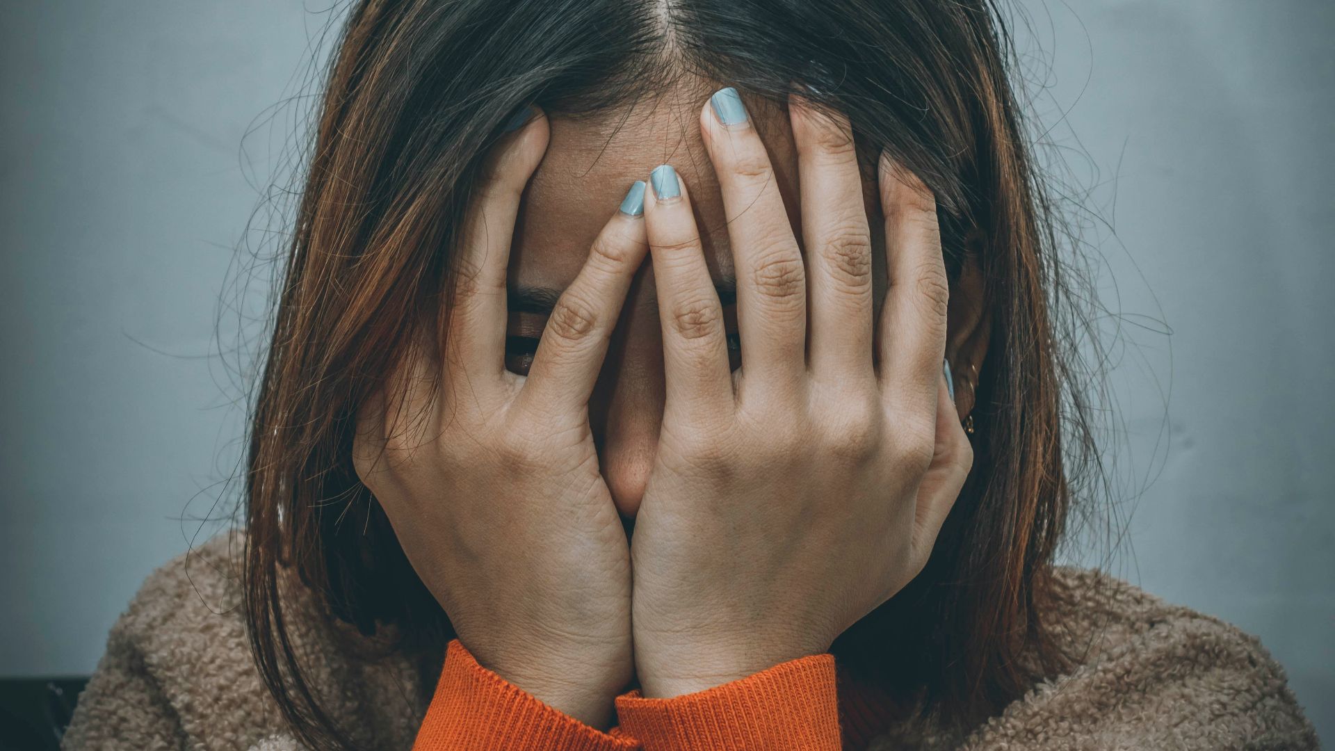 woman in brown sweater covering her face with her hand