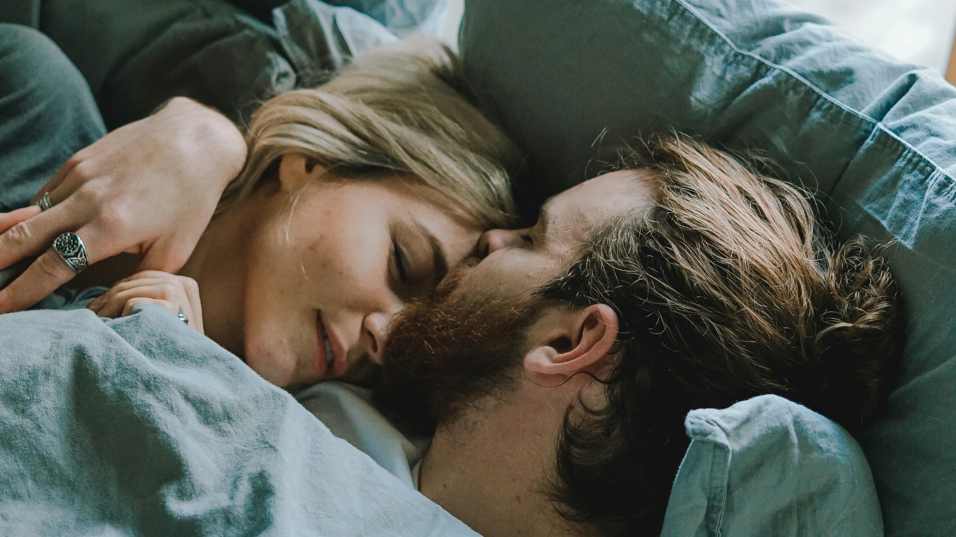 man kissing woman's forehead while lying on bed