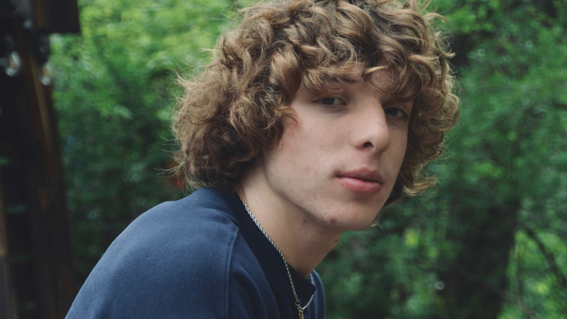 a young man with curly hair sitting on a bench