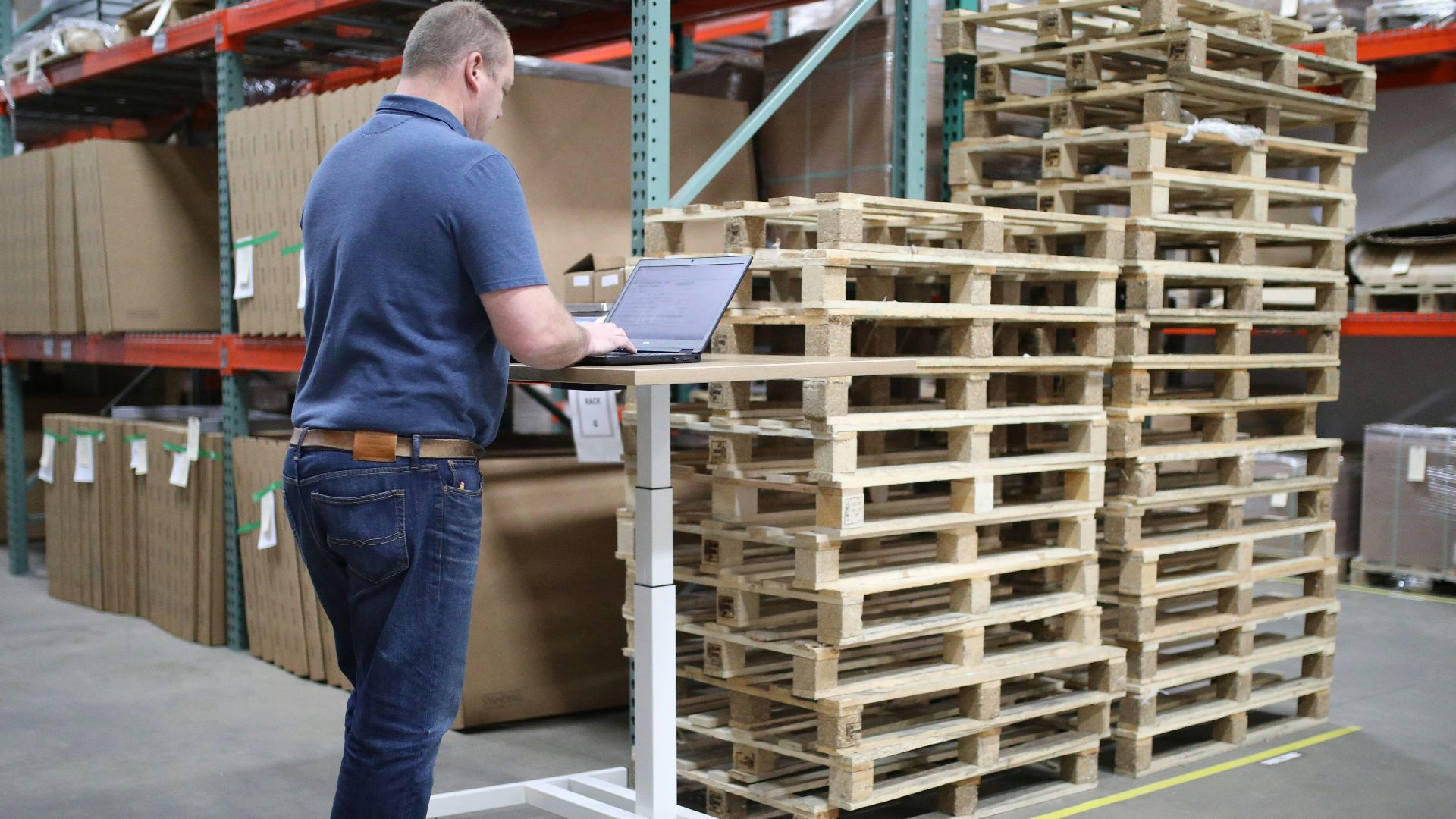 man in blue polo shirt and blue denim jeans standing near brown wooden shelf