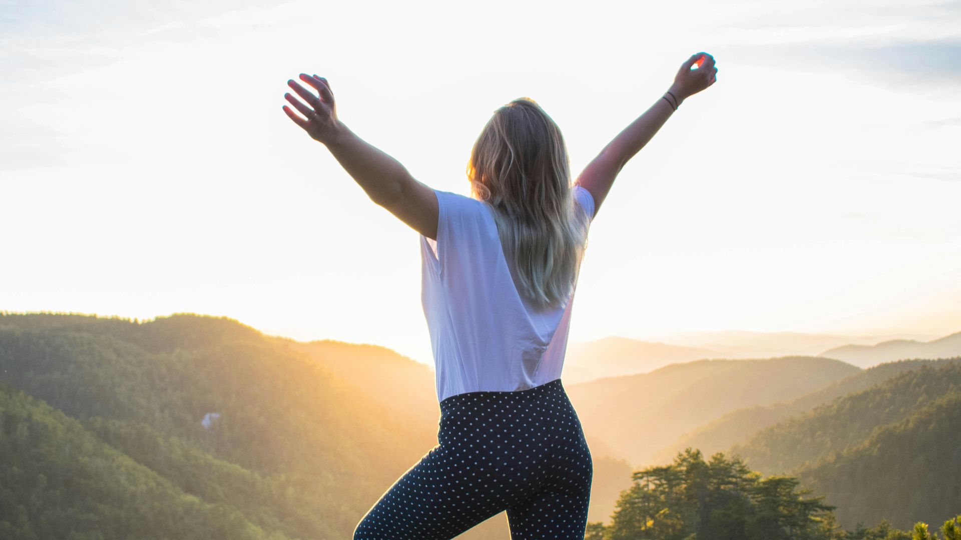 woman in white shirt and black pants standing on rocky mountain during daytime