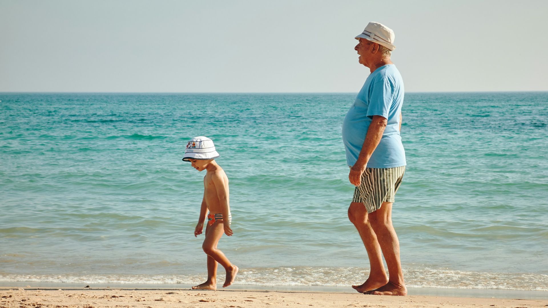 man in blue shirt standing on seashore near boy in white hat